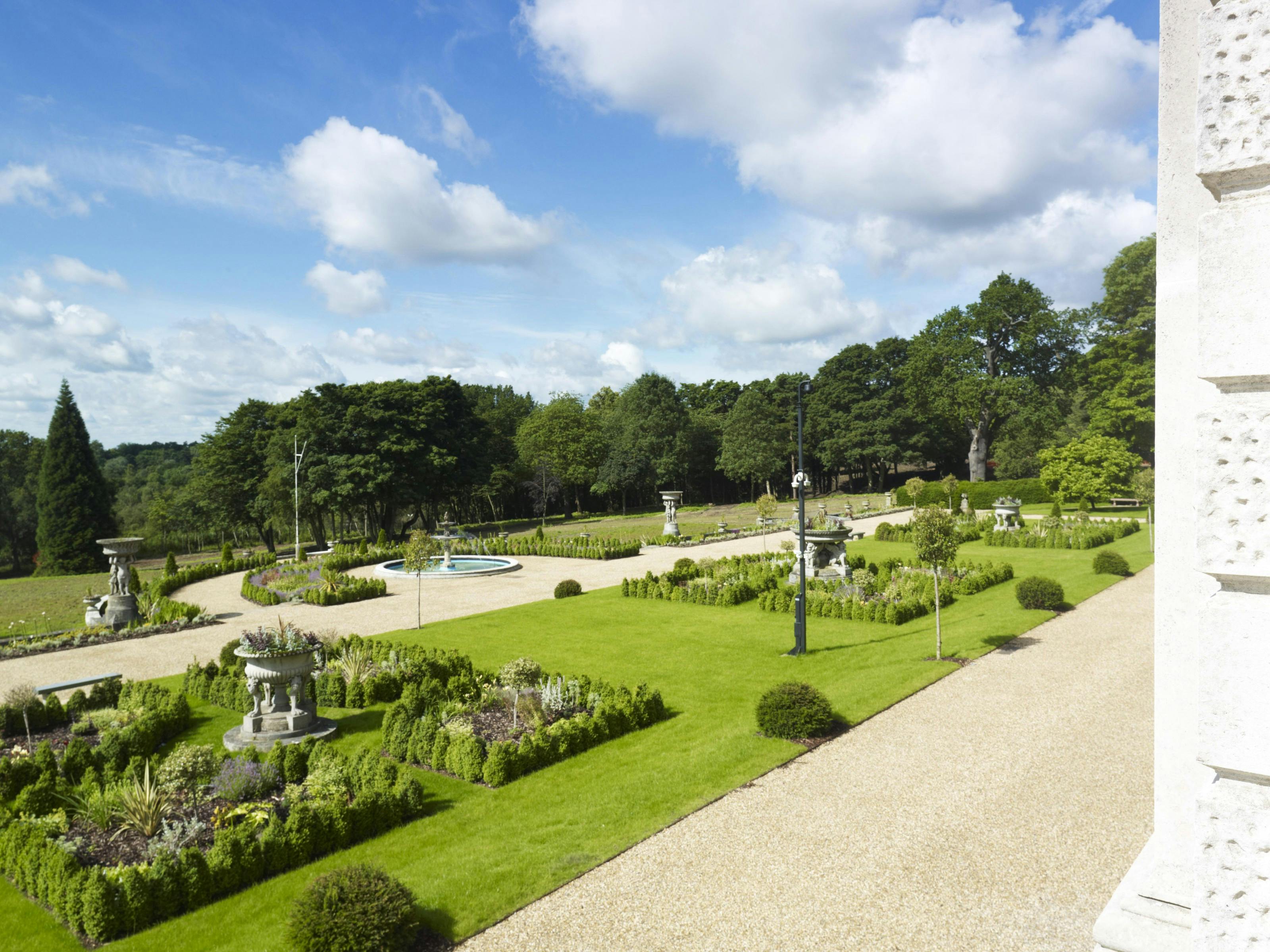 Caption: a large garden with a fountain in the middle of it