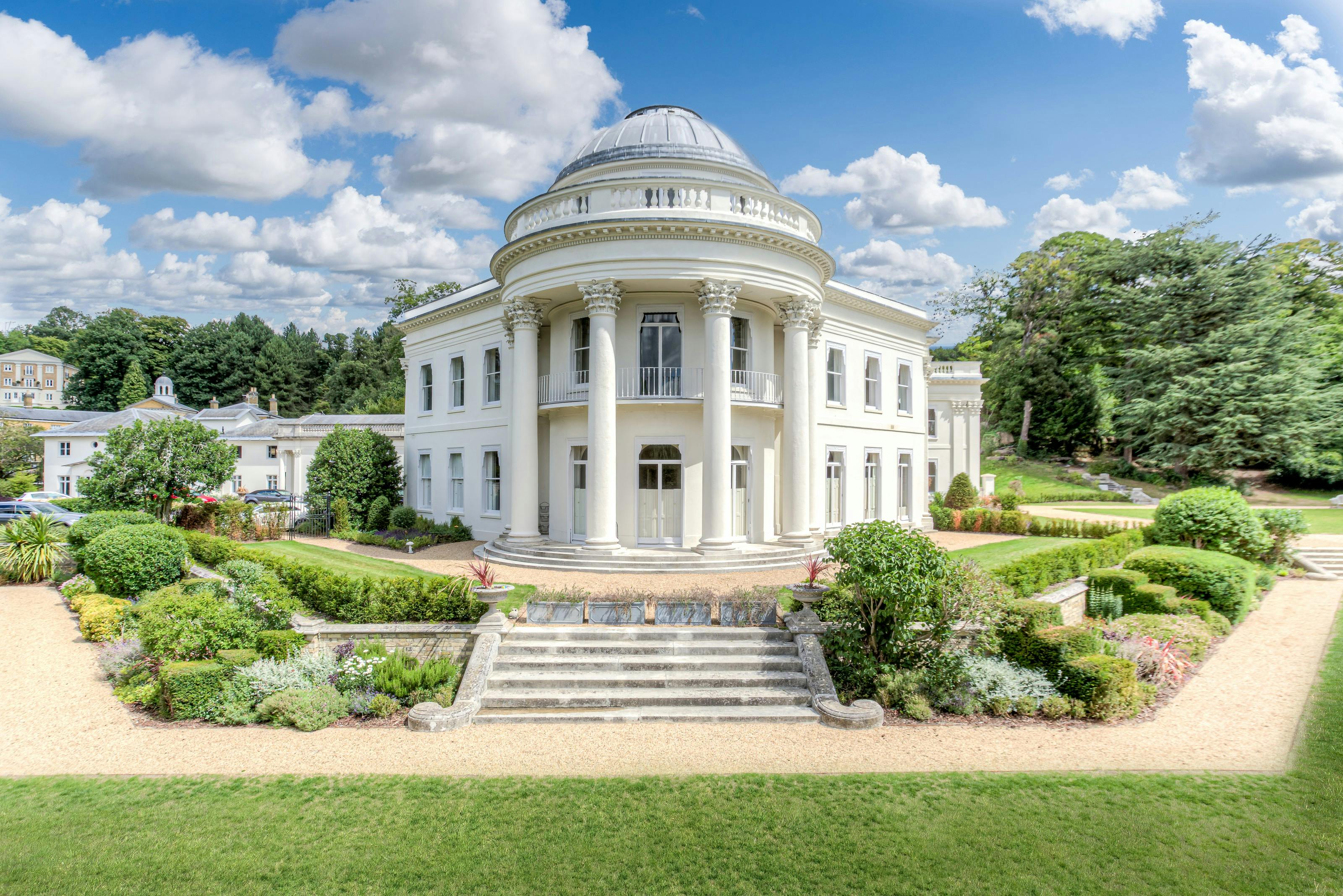 Caption: a large white building surrounded by lush green trees