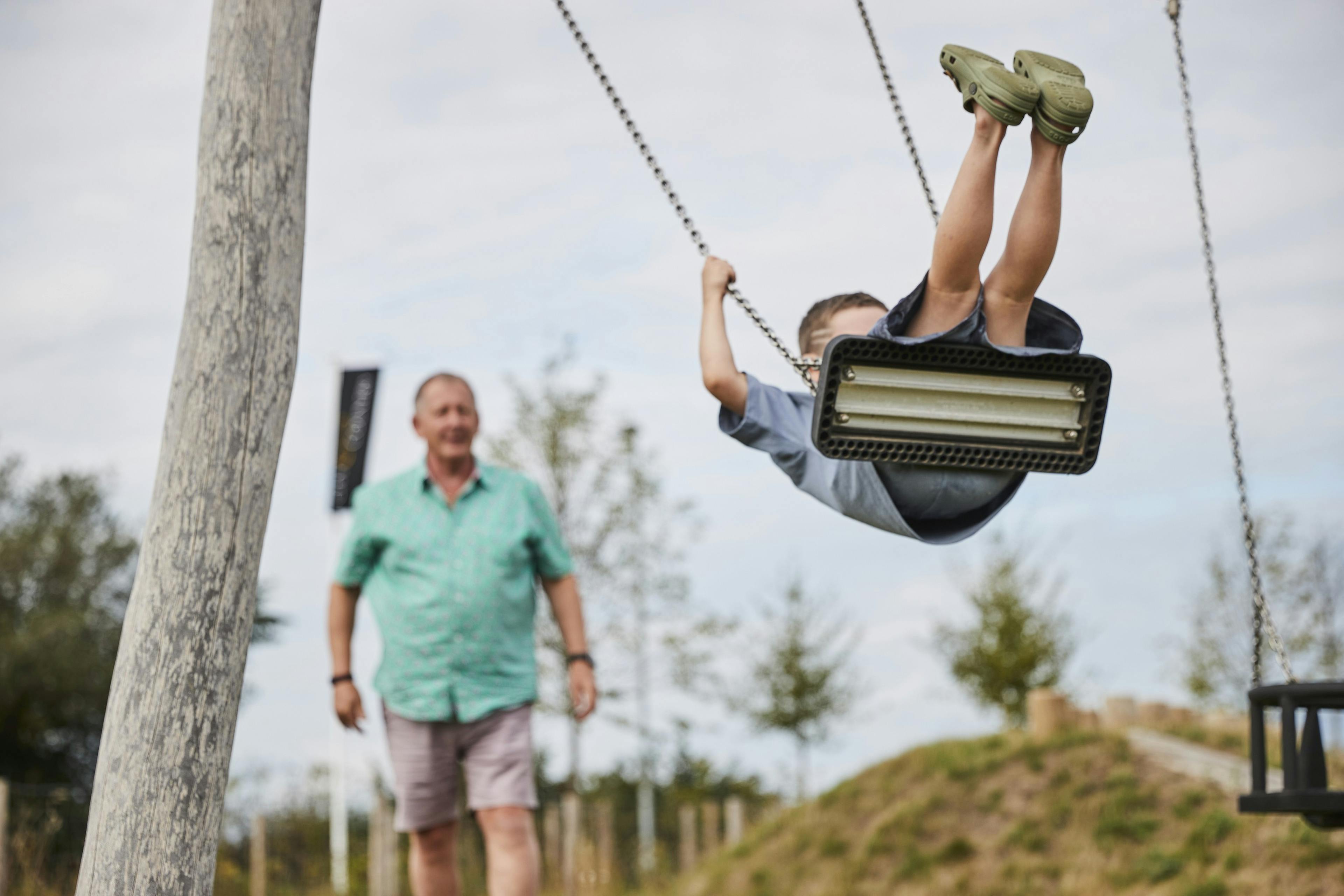 A child on a swing with their grandfather watching from a distance