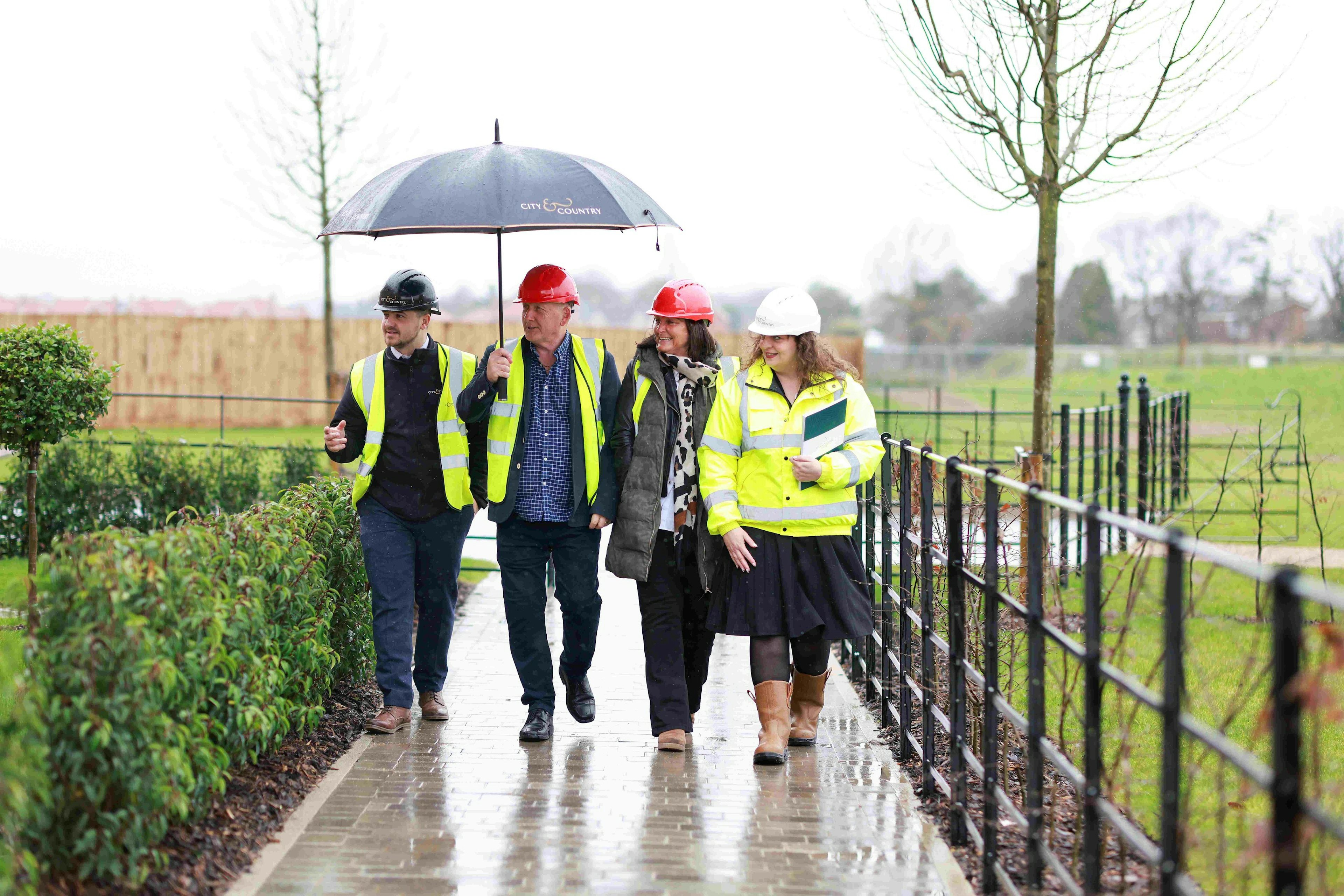 A group of people wearing hard hats walking in the rain under an umbrella