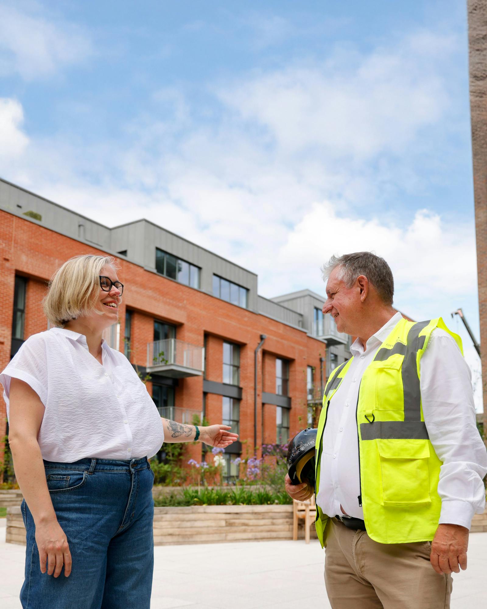 A member of the City & Country team in a high visibility vest having a conversation with a customer outside on a sunny day