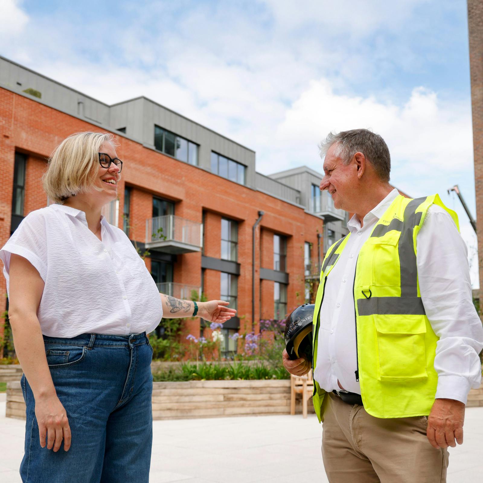 A member of the City & Country team in a high visibility vest having a conversation with a customer outside on a sunny day
