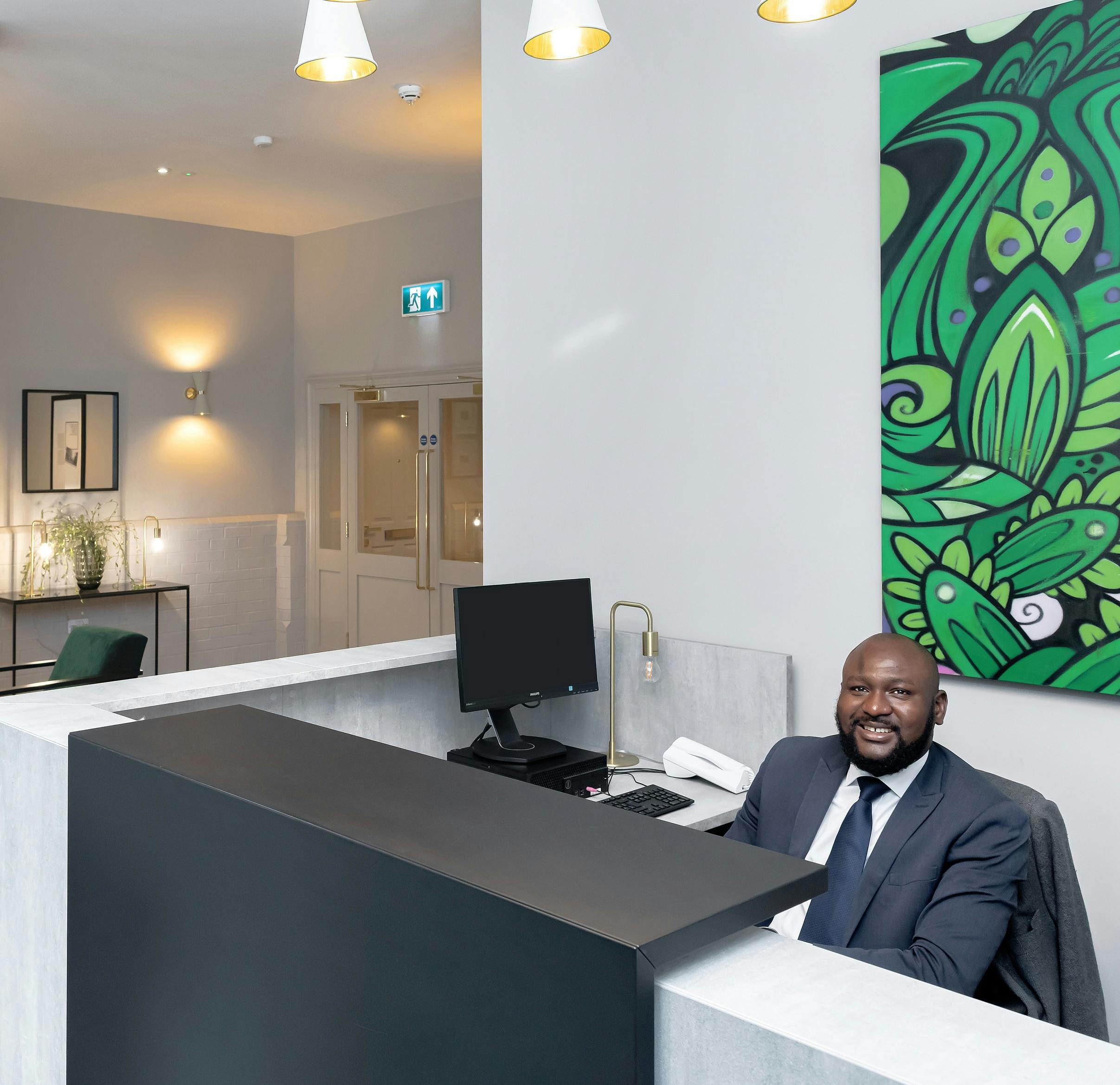 Caption: a man sitting at a desk in front of a painting
