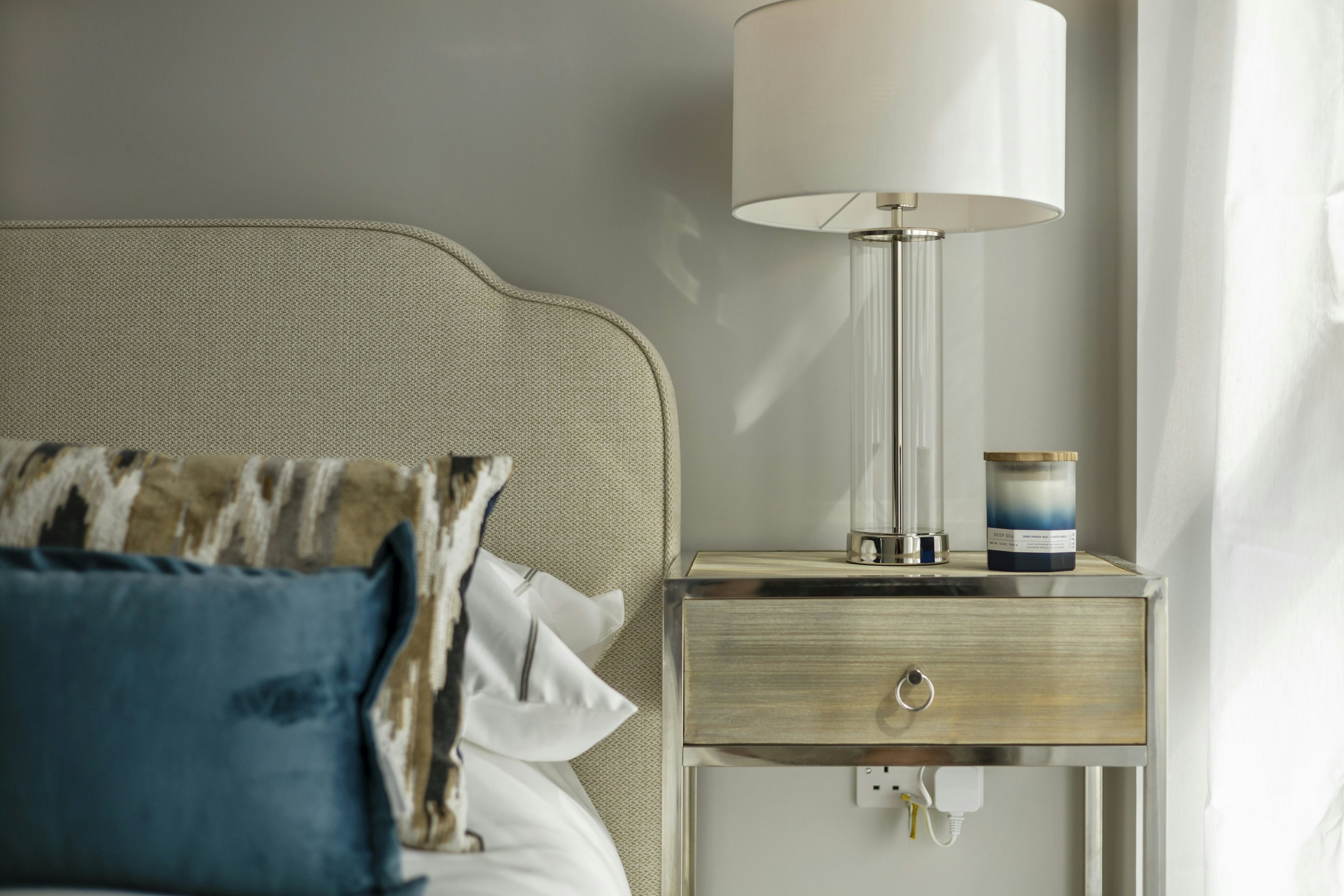 Caption: a nightstand with a lamp on top of it next to a bed