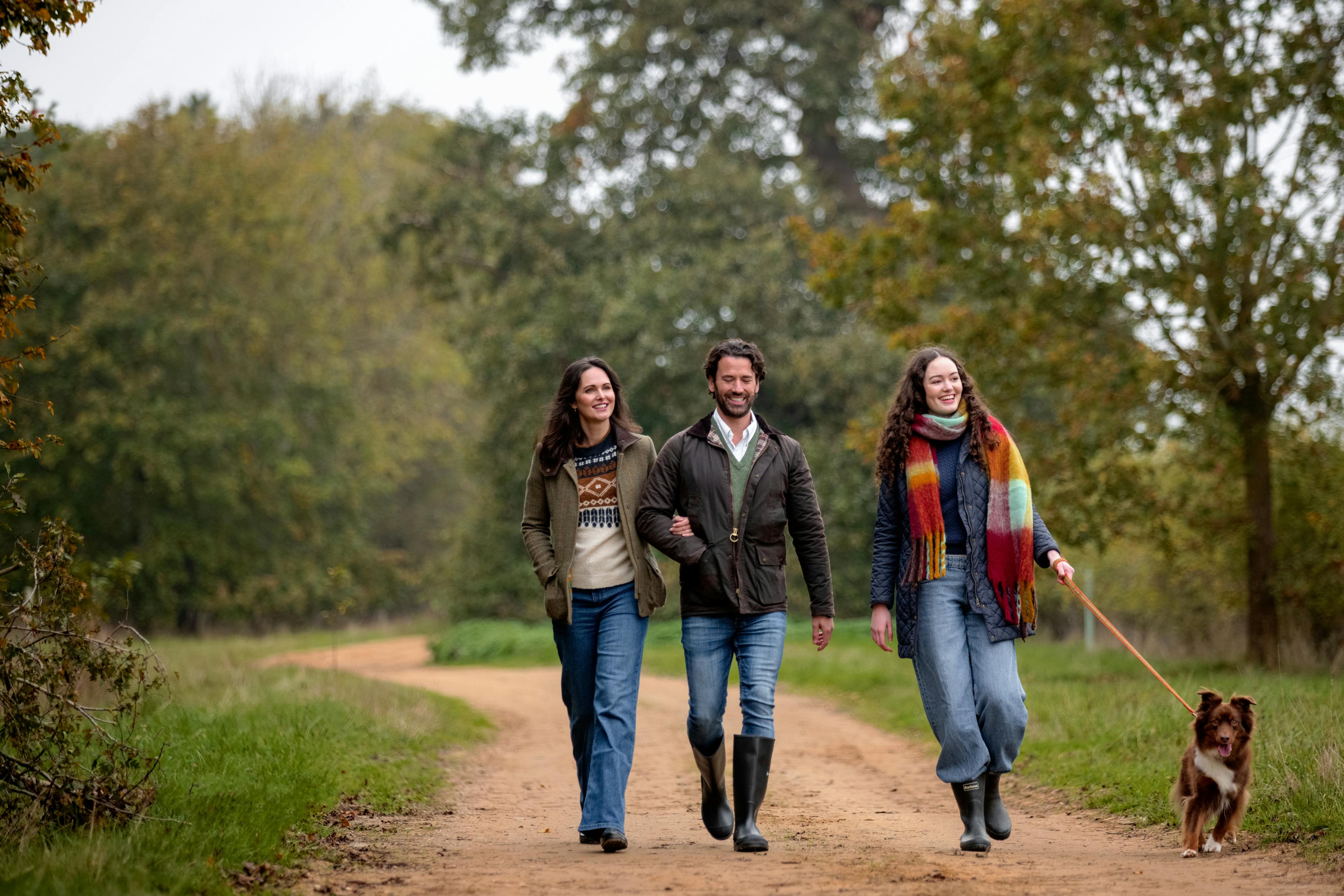 Caption: three people walking down a dirt road with a dog