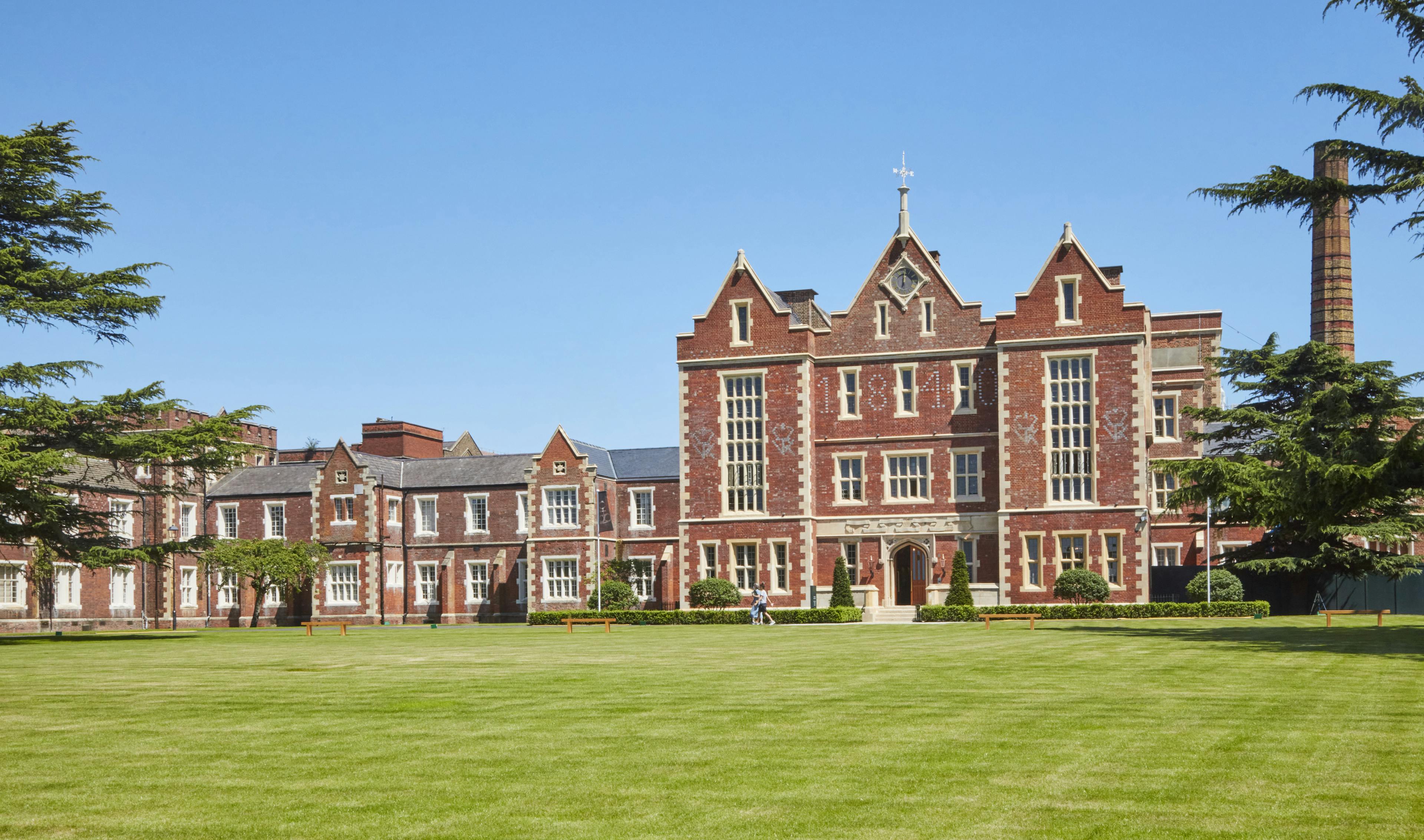 Caption: a large red brick building sitting on top of a lush green field