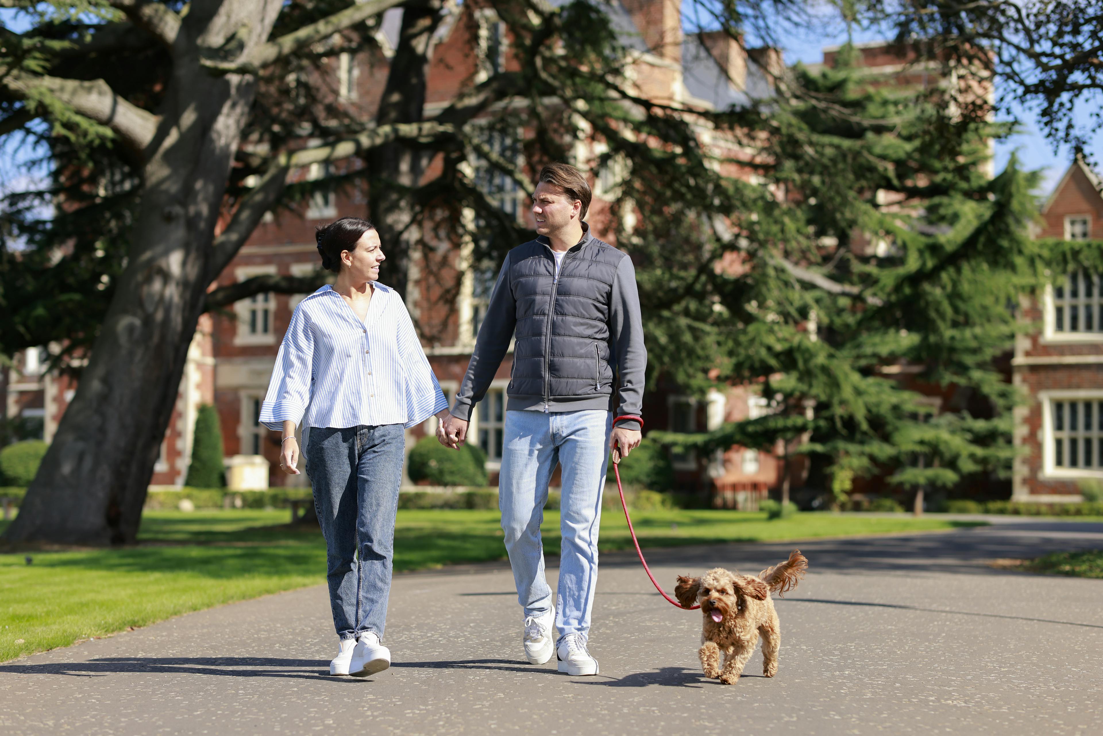 Caption: a man and a woman walking a dog on a leash