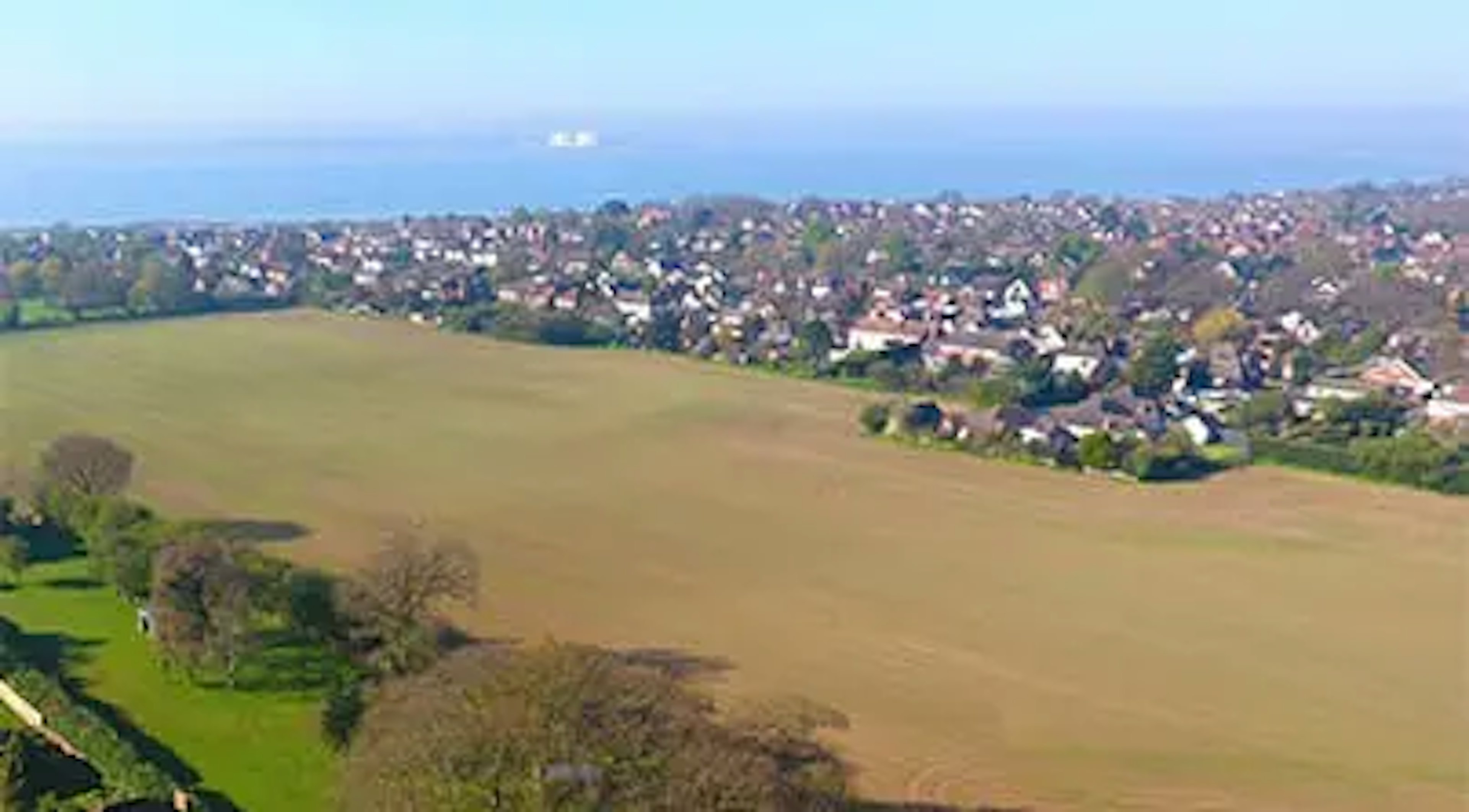 Caption: a bird's eye view of a green field with houses in the background