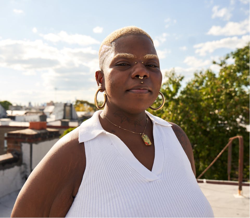 A woman with blonde short hair wearing a white top and jewelry smiles on top of a rooftop.