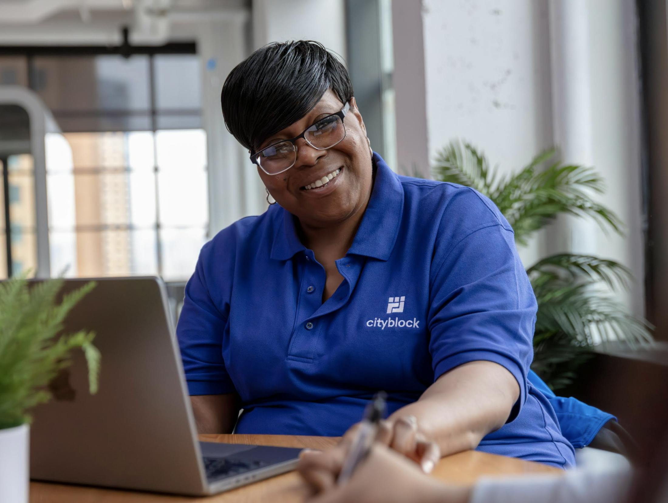Community health partner Catina Purvis-Johnson sits with laptop while wearing a blue polo and smiling.