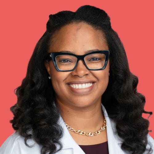 Woman smiles while wearing a white coat and black glasses.