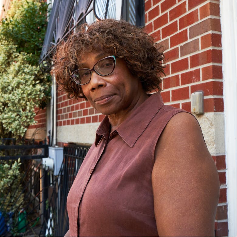 A woman wearing purple sleeveless blouse wearing glasses smilies.