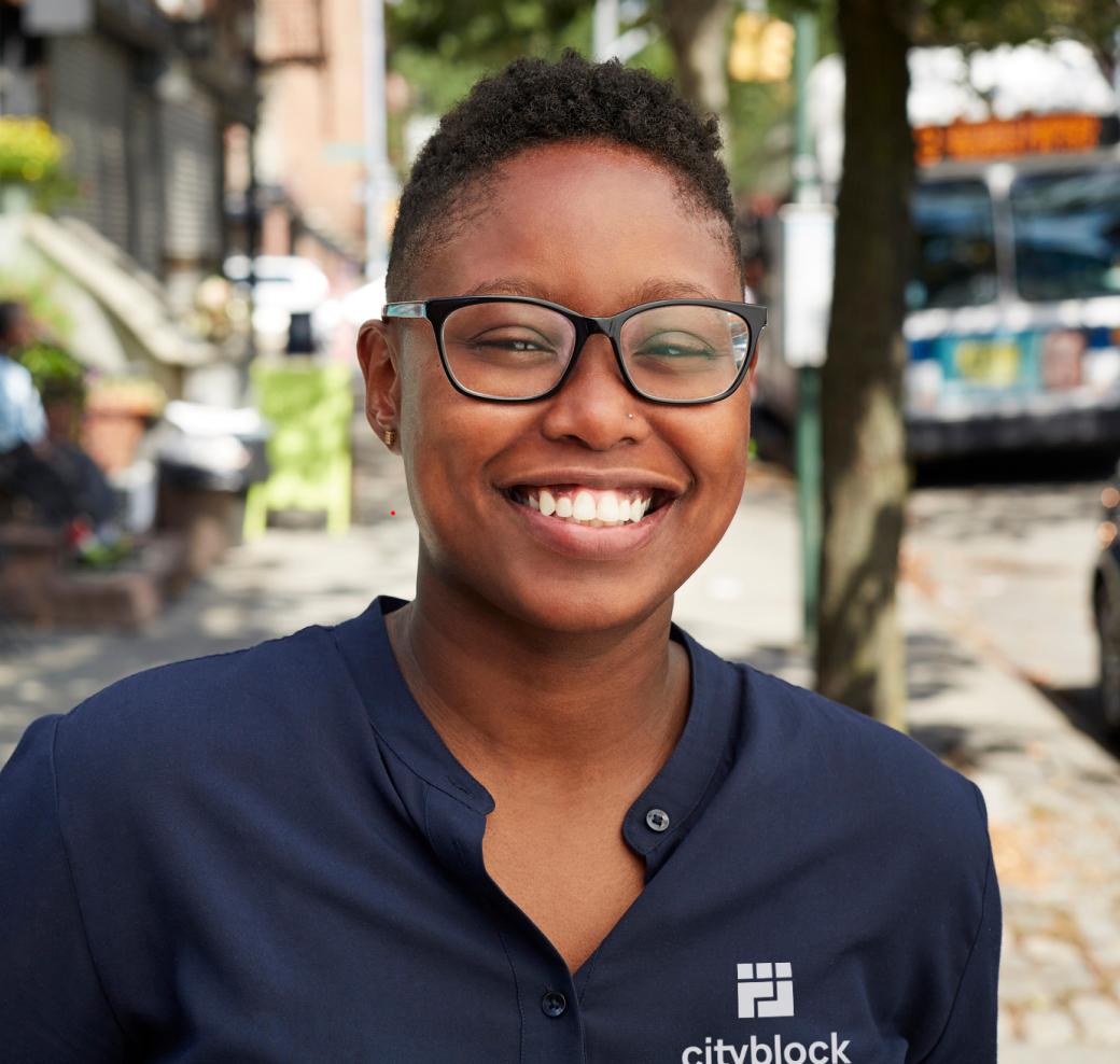 Image of person wearing a navy blue Cityblock logo shirt while smiling and wearing glasses