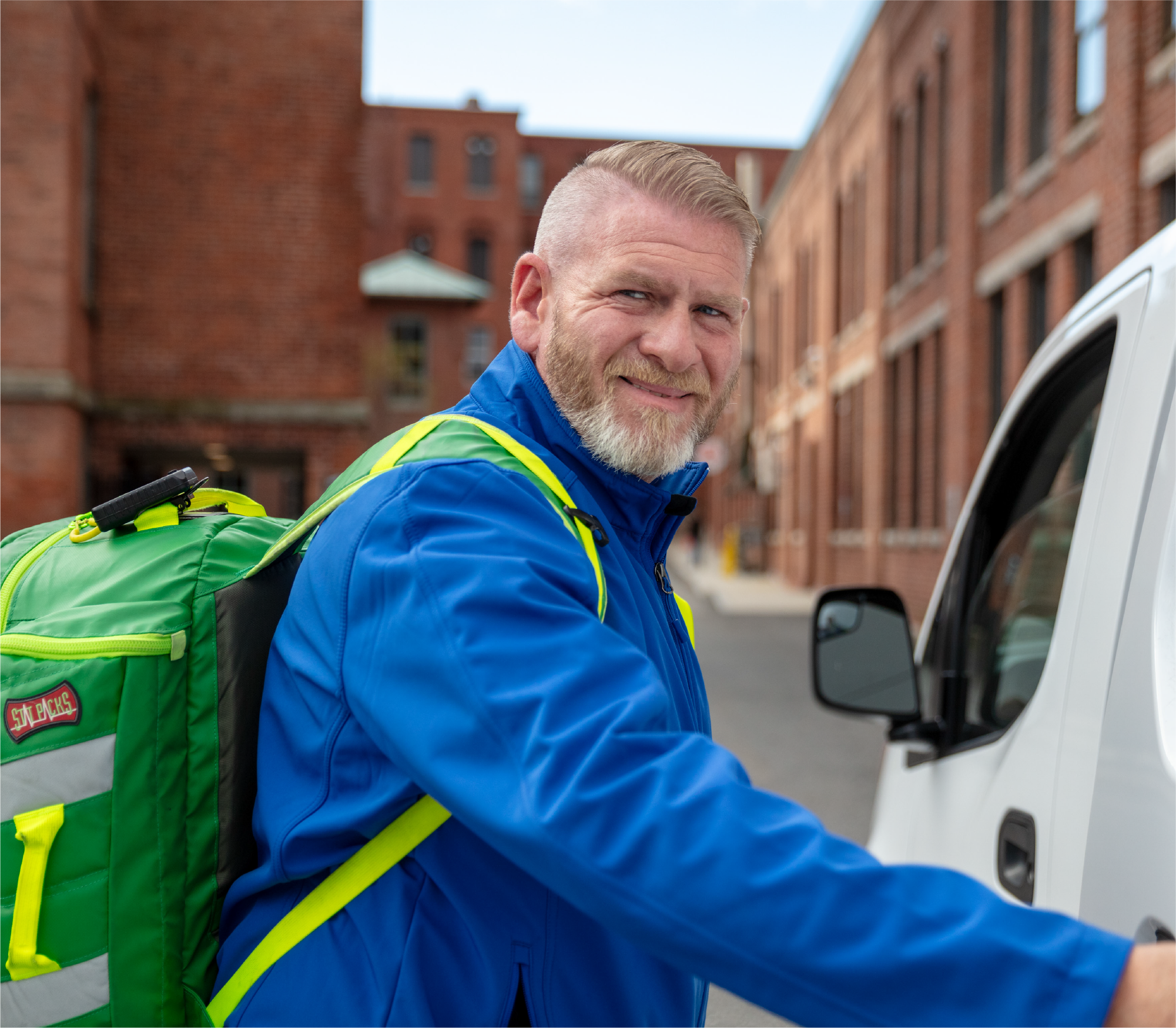 Urgent care community care clinician wears a blue jacket while opening van door.
