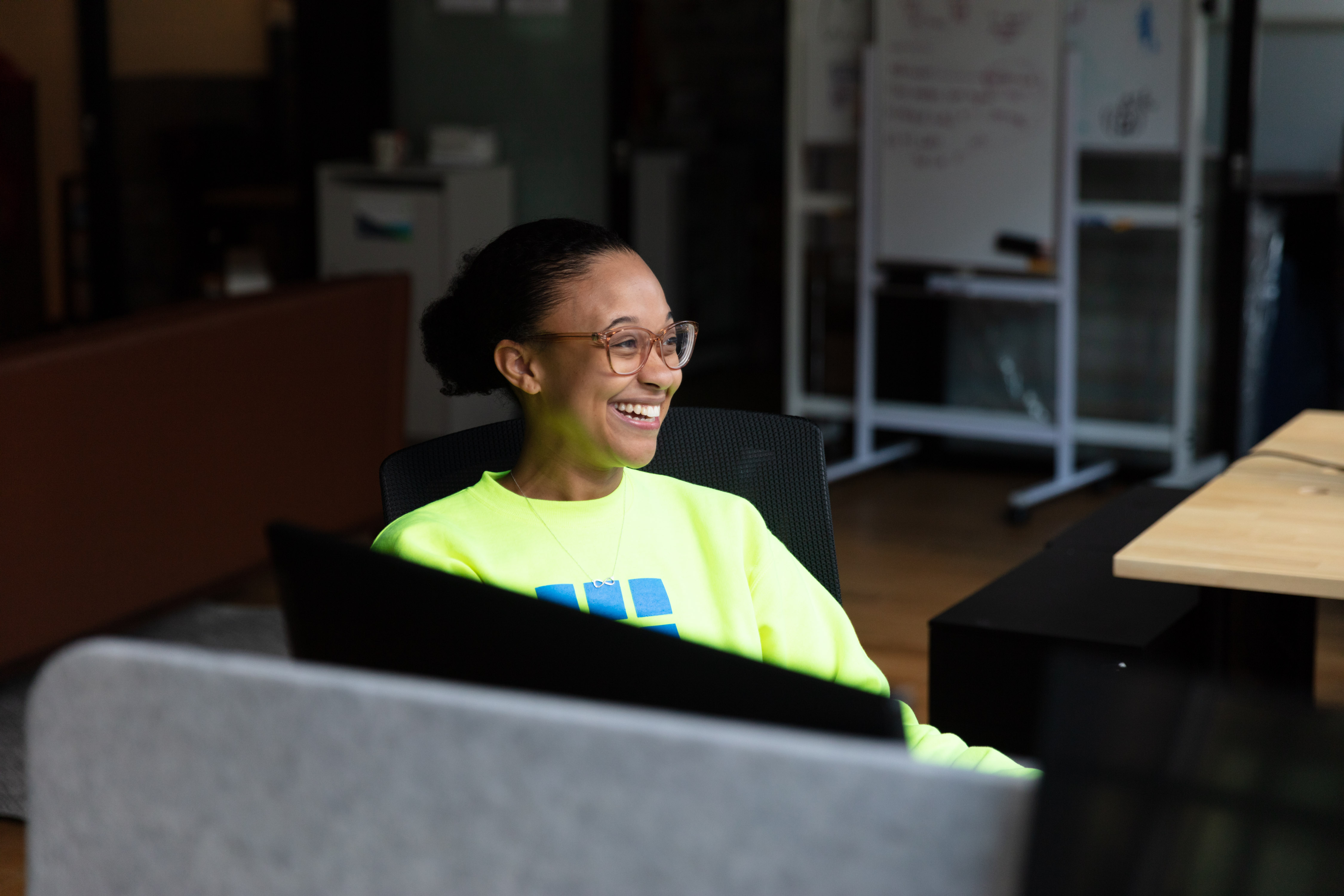 Smiling woman with glasses witting in a chair looking off to the side