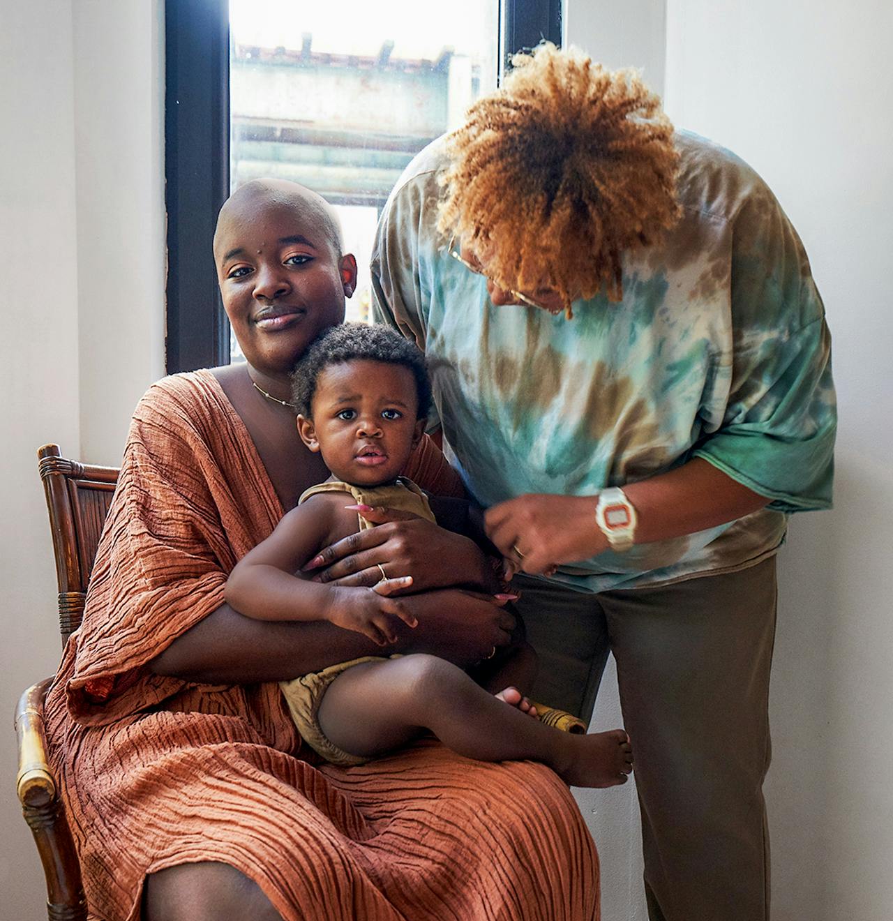Portrait image of two women wearing orange and green smiling holding a baby.