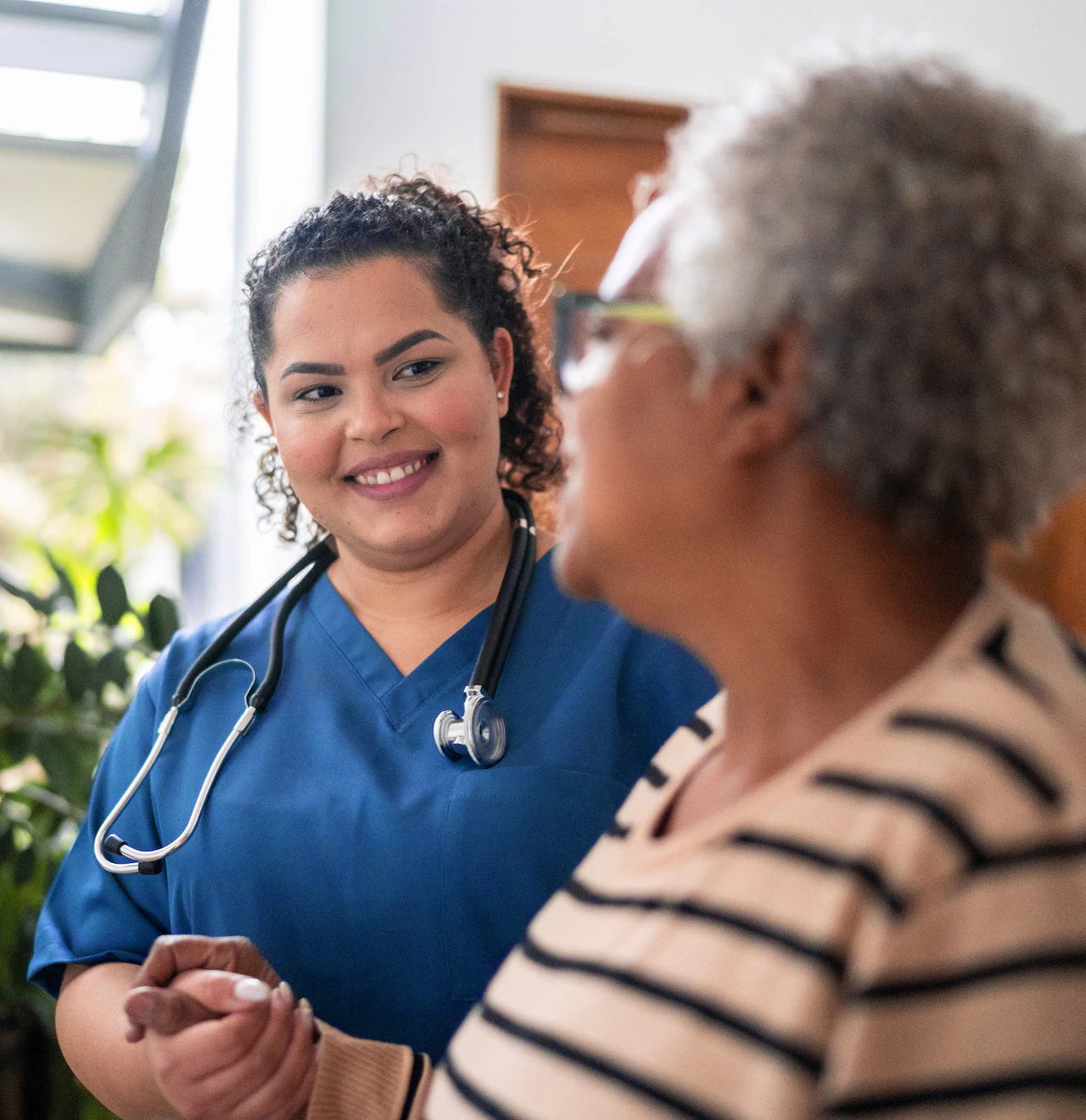 Healthcare worker in blue scrubs helps elderly woman while smiling.