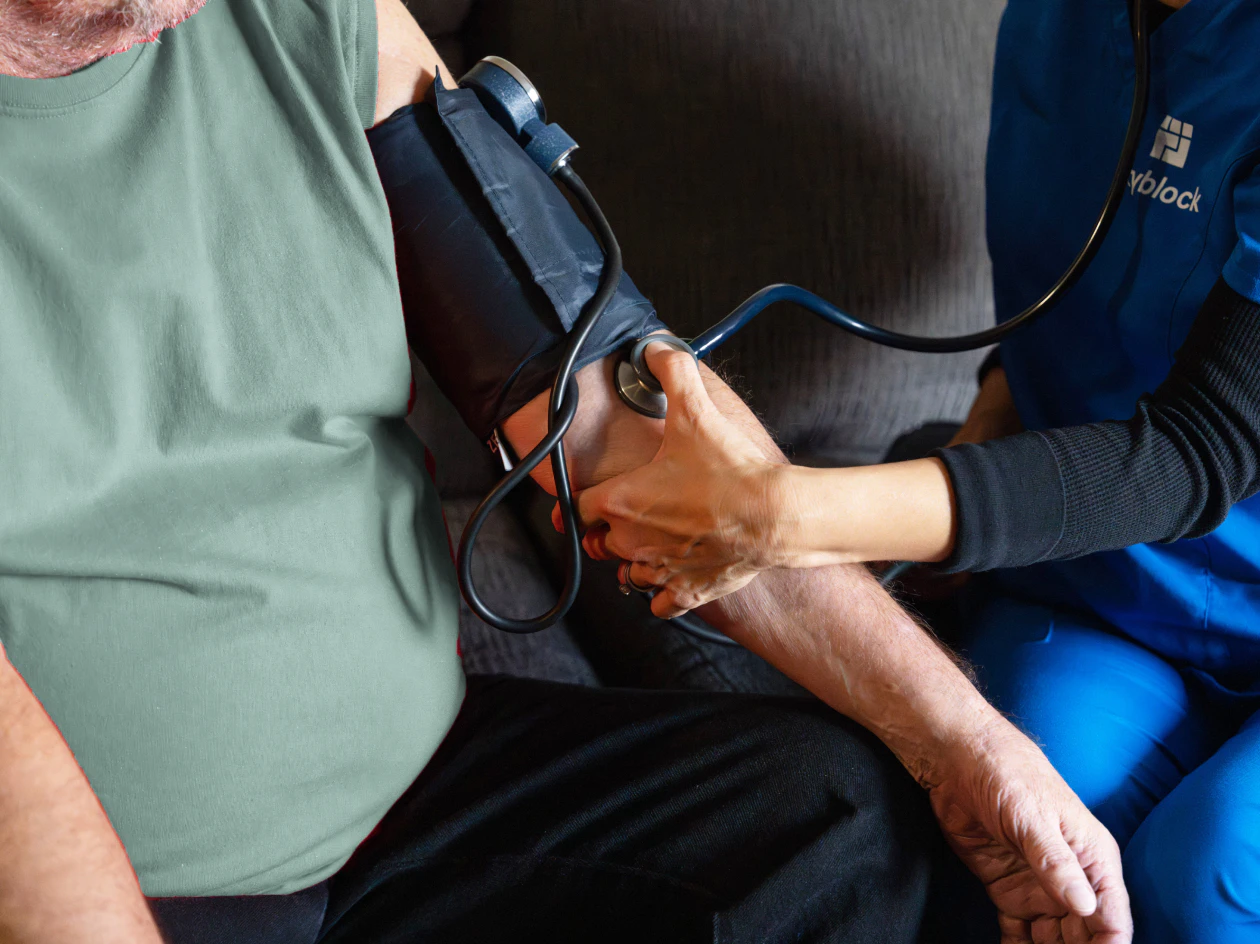 Image of a nurse in blue scrubs taking a member's blood pressure using a manual cuff and stethoscope.