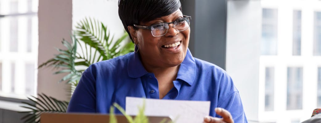 Woman wearing blue shirt and glasses smiles while holding a document.