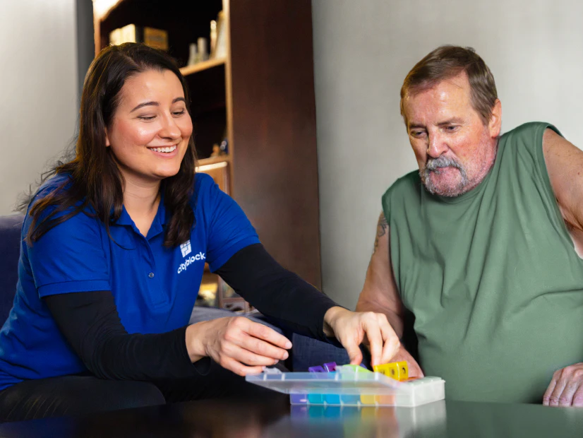 Image of a community health partner helping an older man organize his daily pills into a colorful plastic pill organizer.