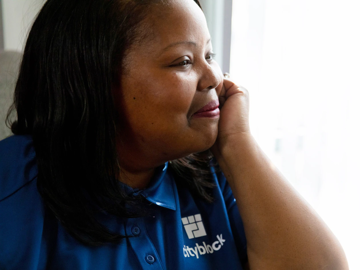 Image of a community health partner wearing a blue Cityblock polo shirt looking out a bright window.