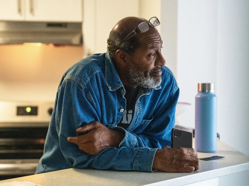 Image of a member with glasses on his head leaning on a kitchen counter holding a smartphone next to a water bottle.