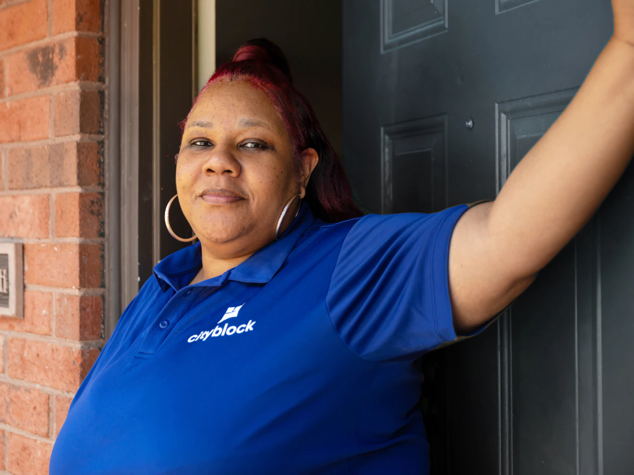 Image of a community health partner in a blue polo shirt leaning against an open doorway and looking directly into the camera.