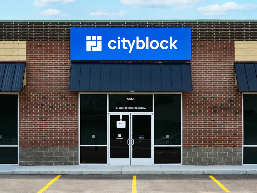 Image of the exterior of a Cityblock clinic featuring a blue logo sign, glass front doors, dark awnings, and brick walls.