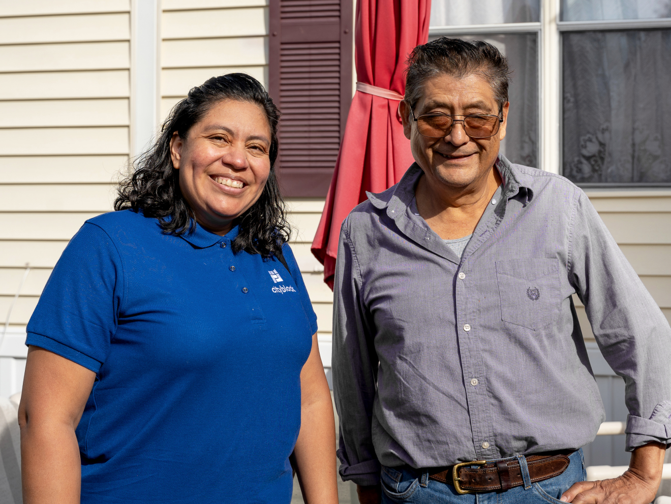 Woman wearing a blue polo with Cityblock logo and man with long sleeve shirt smile while standing.