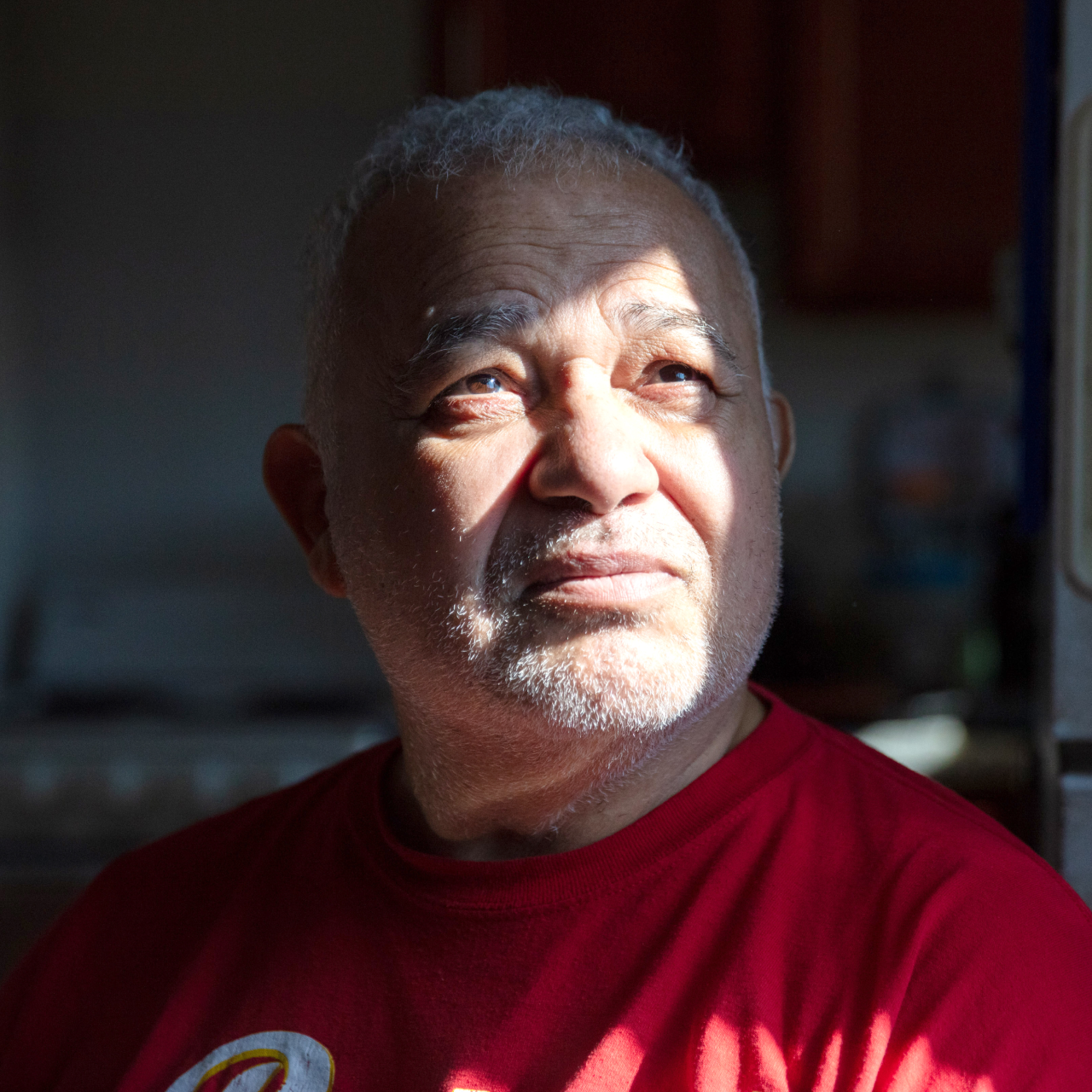 Man wearing a red t-shirt looks into distance with sunshine shadow on face.