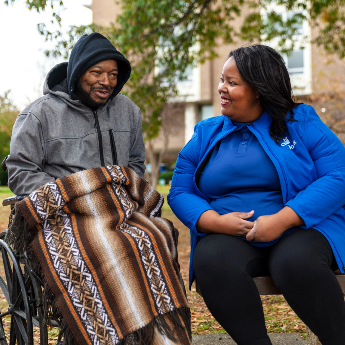 Man in wheelchair smiles together with a woman sitting at the park.