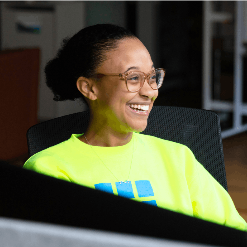 Woman wearing florescent crewneck and glasses smiles.