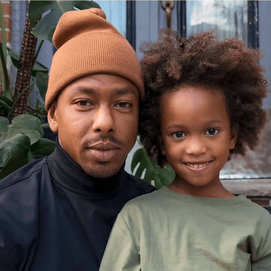 Person with a child wearing a black turtleneck and green shirt sits on stoop stairs smiling.