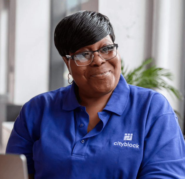 Social care employee wears blue polo with Cityblock logo while smiling proudly.