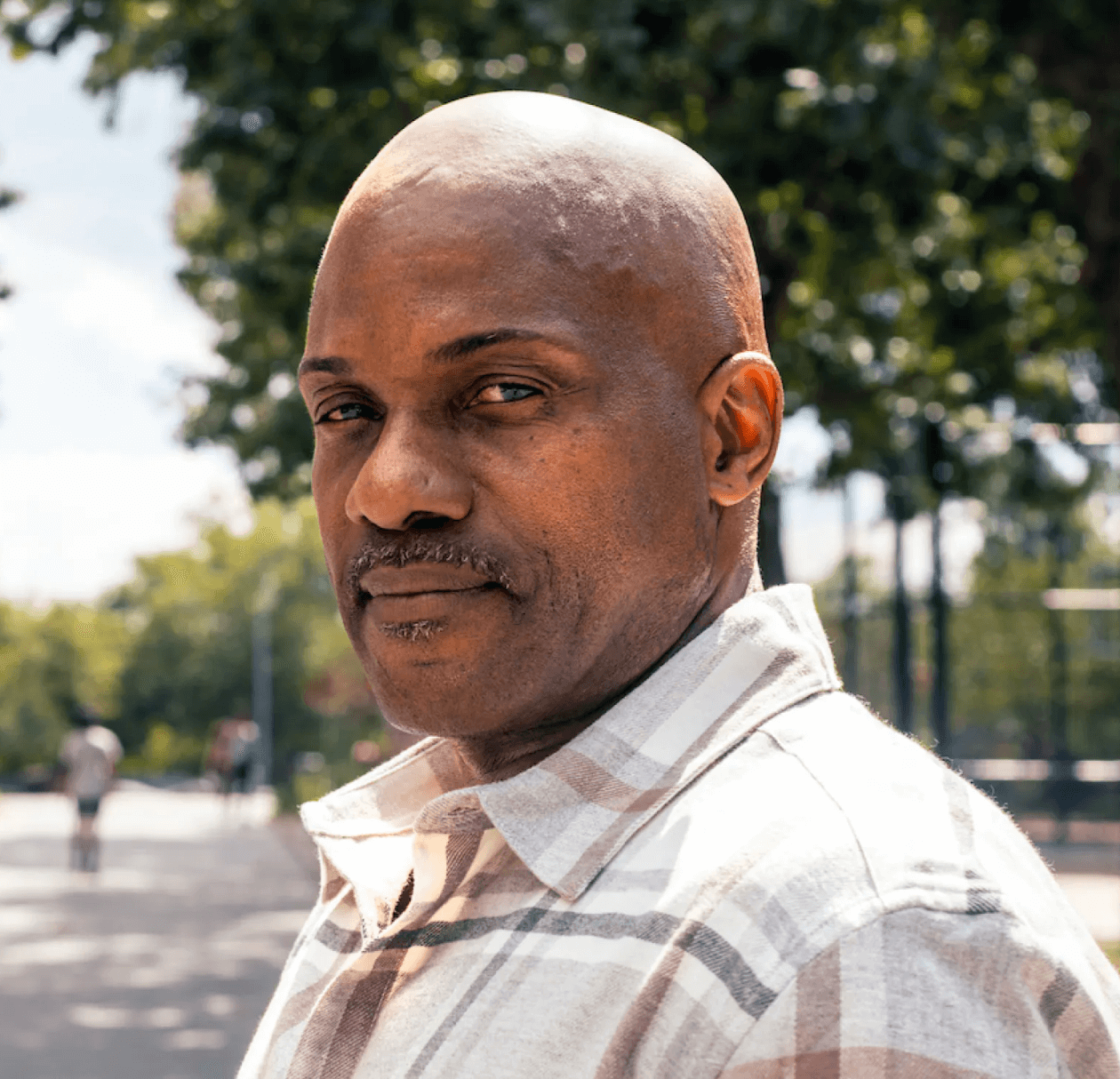 Portrait image of black man looking optimistic at the park with sun shining.