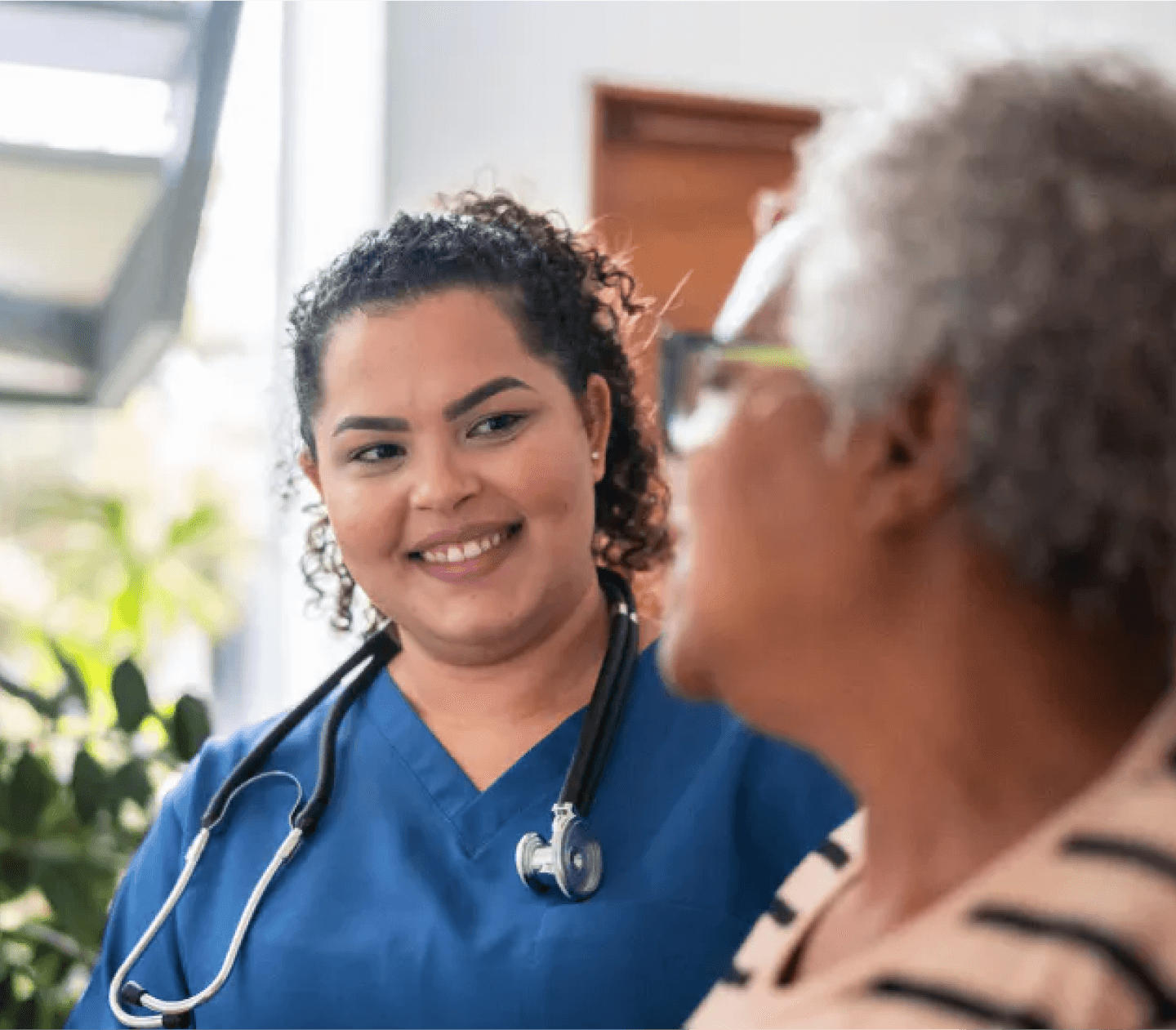 Healthcare worker in blue scrubs helps elderly woman while smiling.