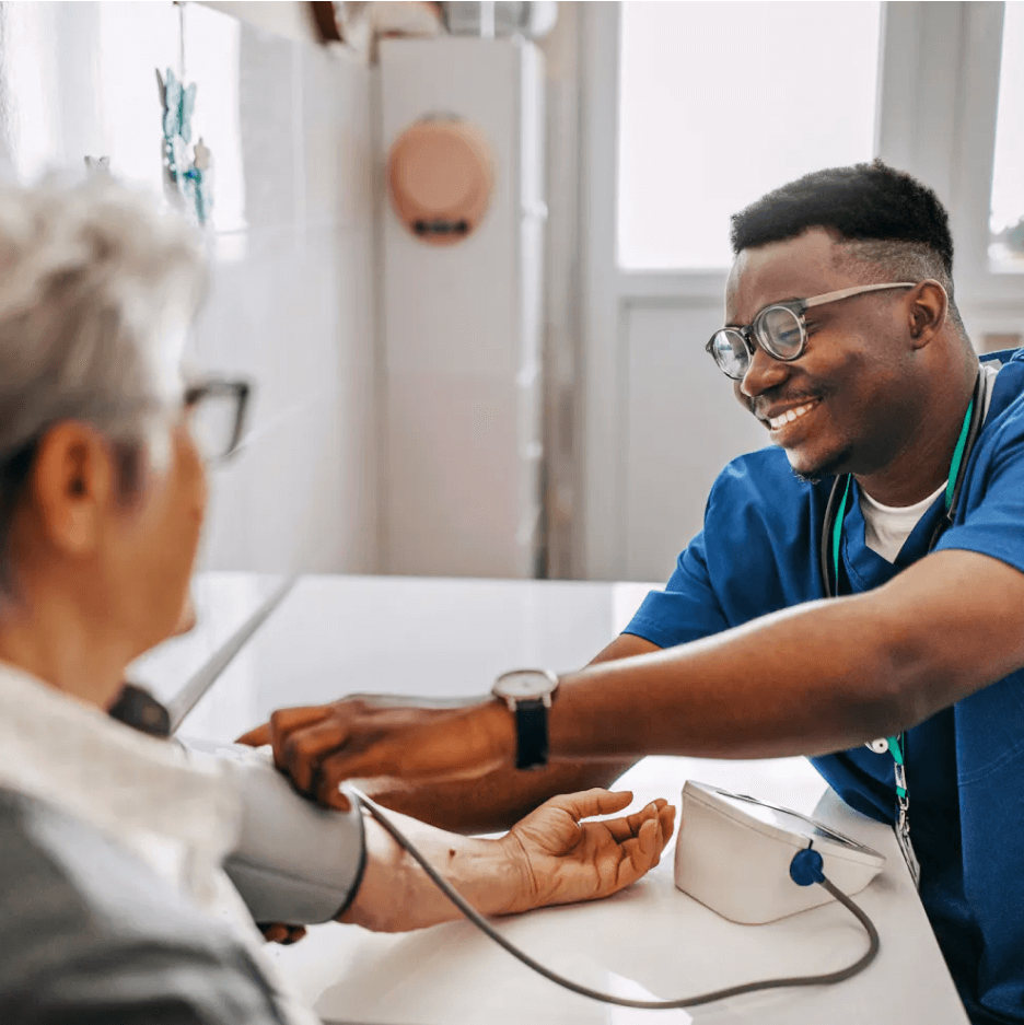 Provider wearing blue scrubs checking the blood pressure of person at home