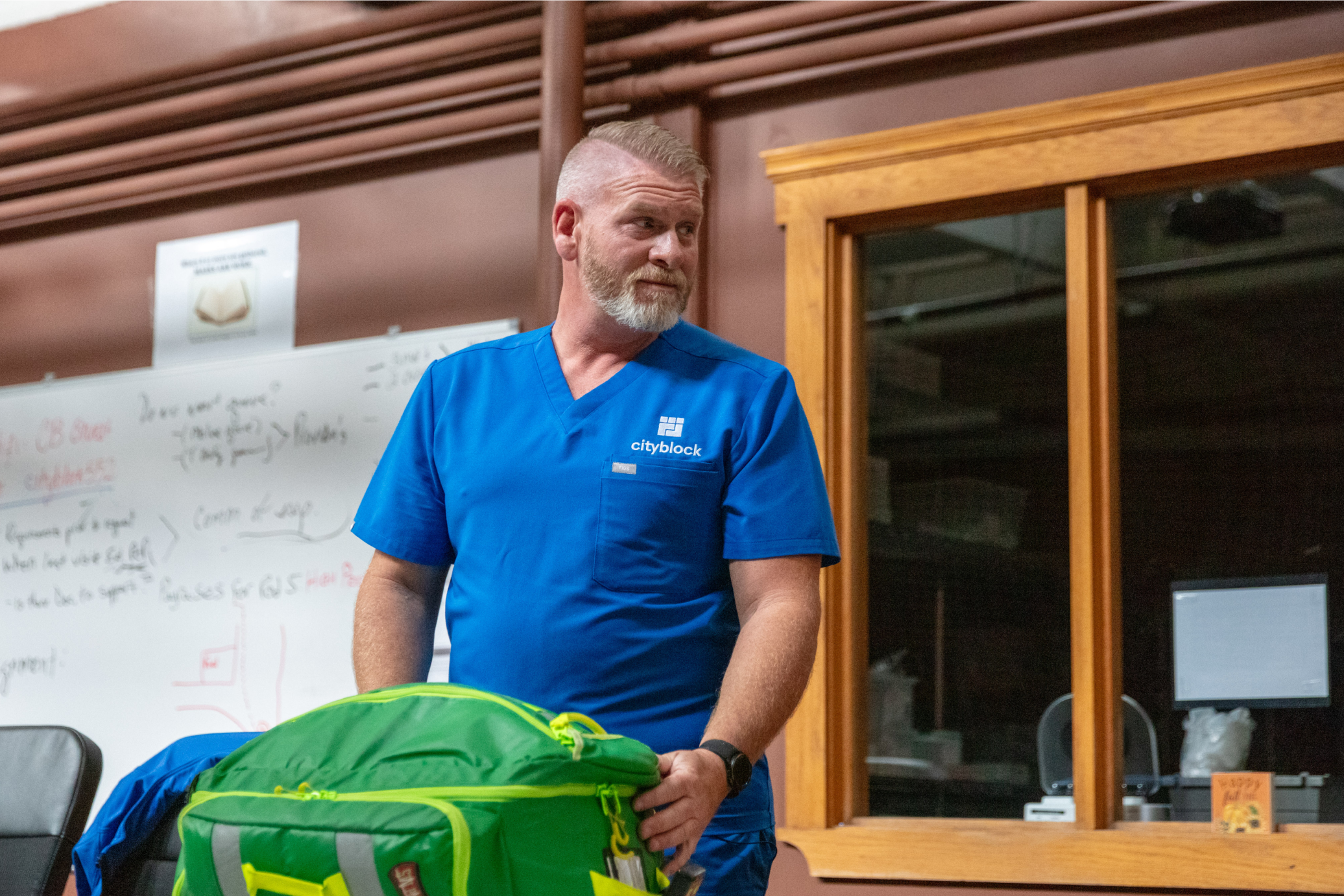 Cityblock care team member holds a green bag while wearing blue scrubs.