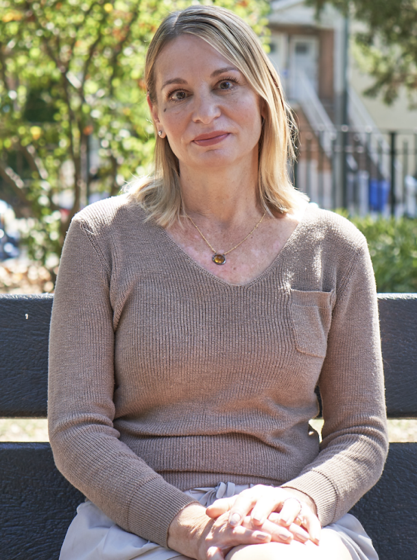 Portrait of a woman sitting at a park bench with a tan sweater.