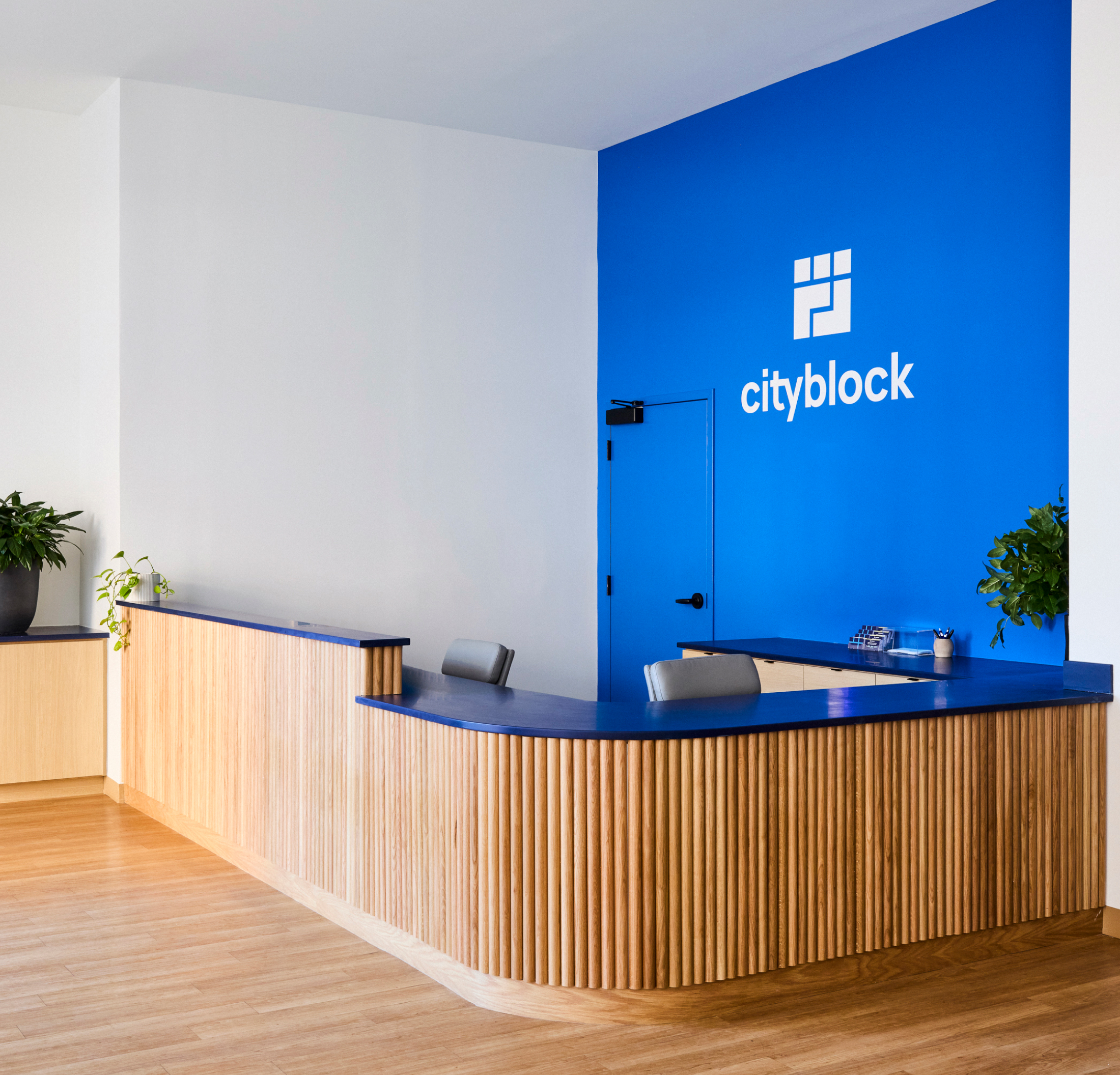 Front desk with warm wood and a blue Cityblock logo wall.