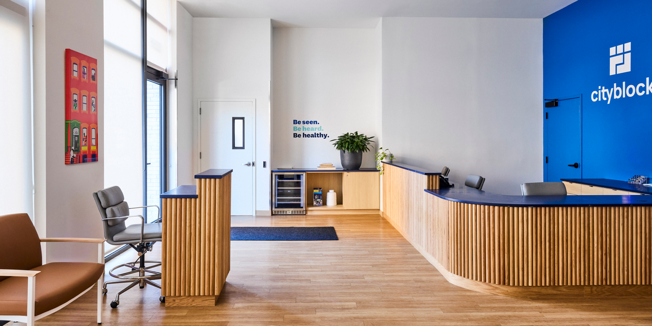 Reception area with front desk with warm wood and wall art that says "Be seen. Be heard. Be healthy."