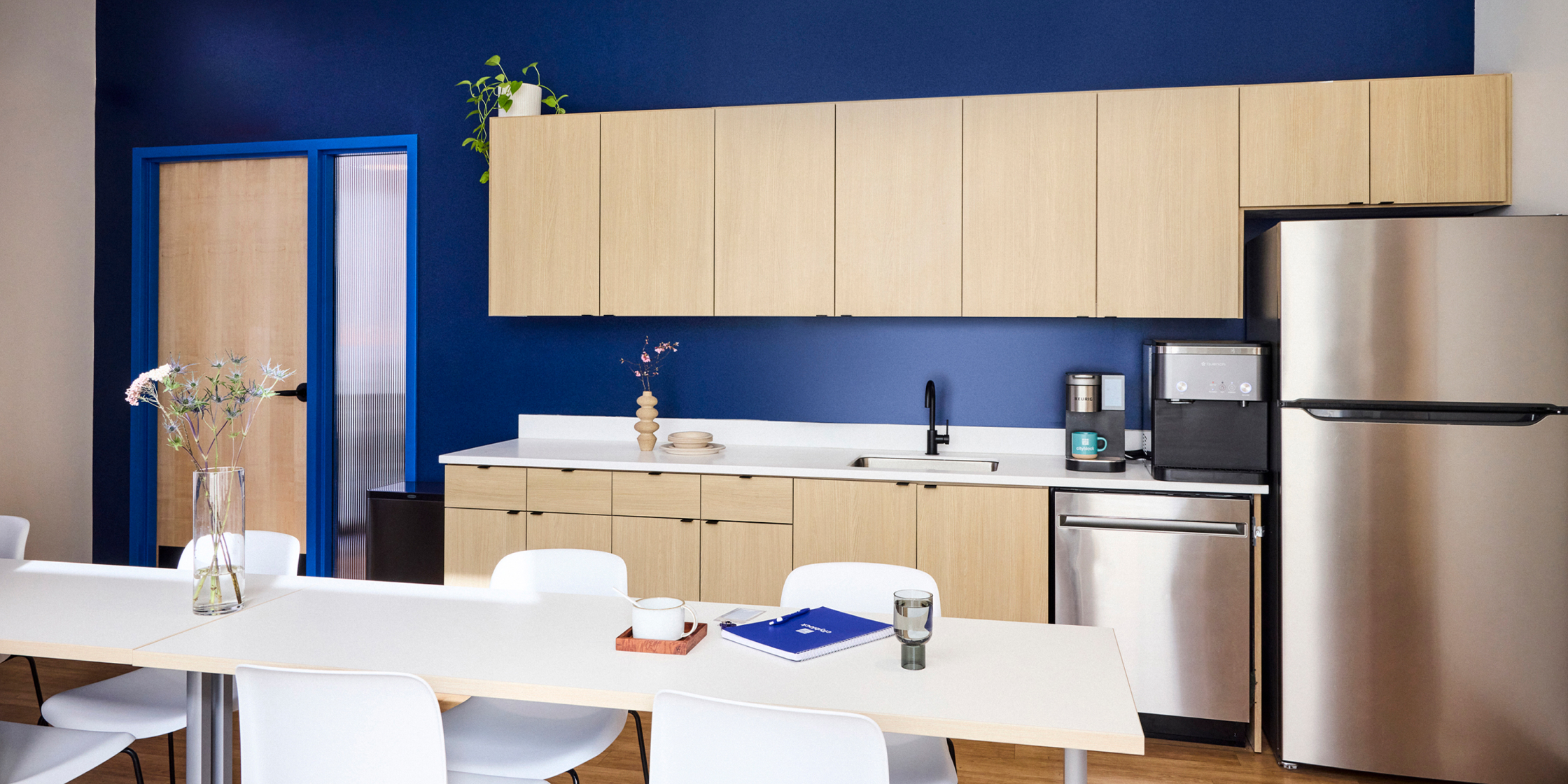 Community room with a white dining table and kitchen area with light wood.