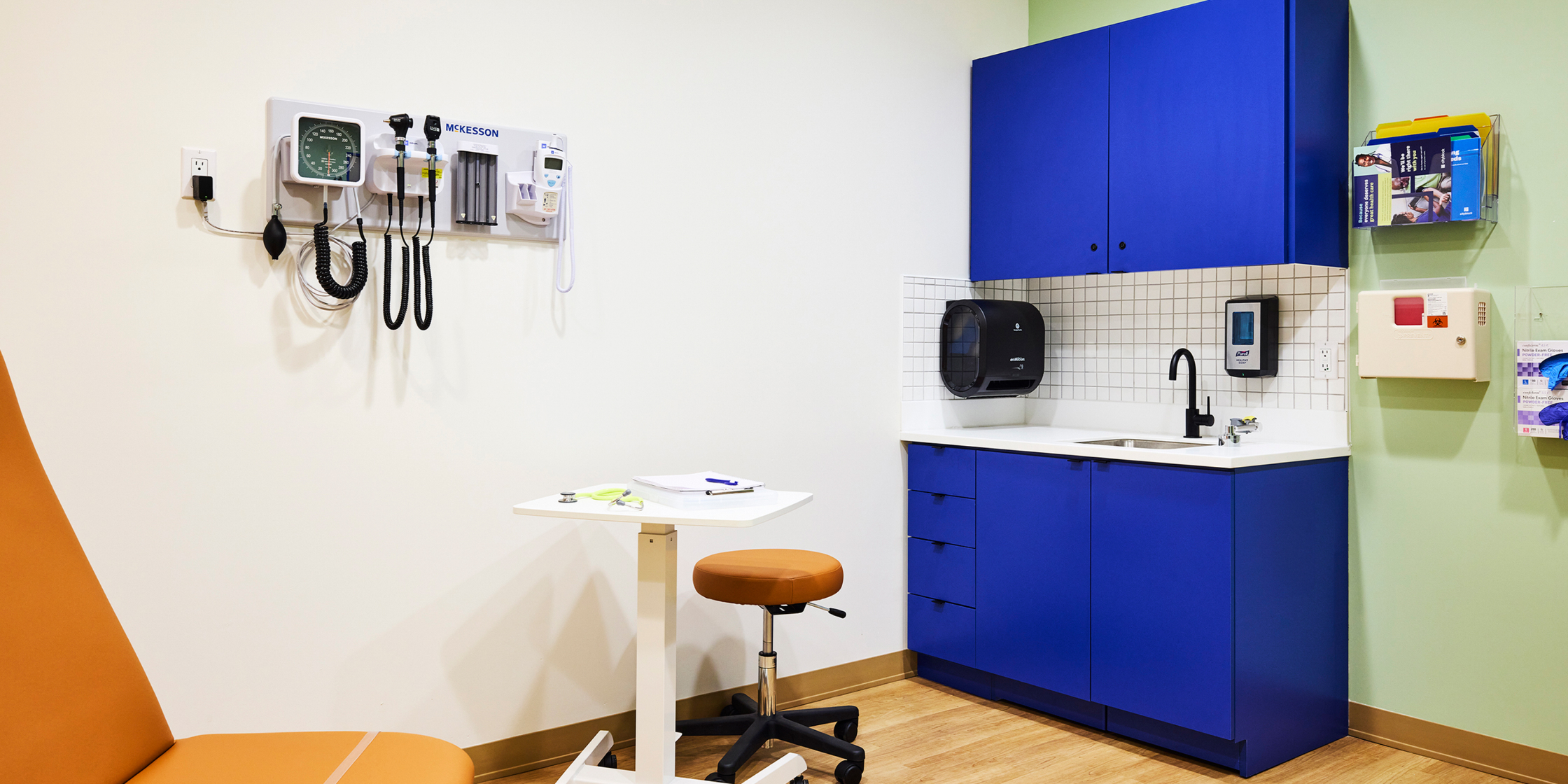 Exam room with tan furniture and blue cabinets.