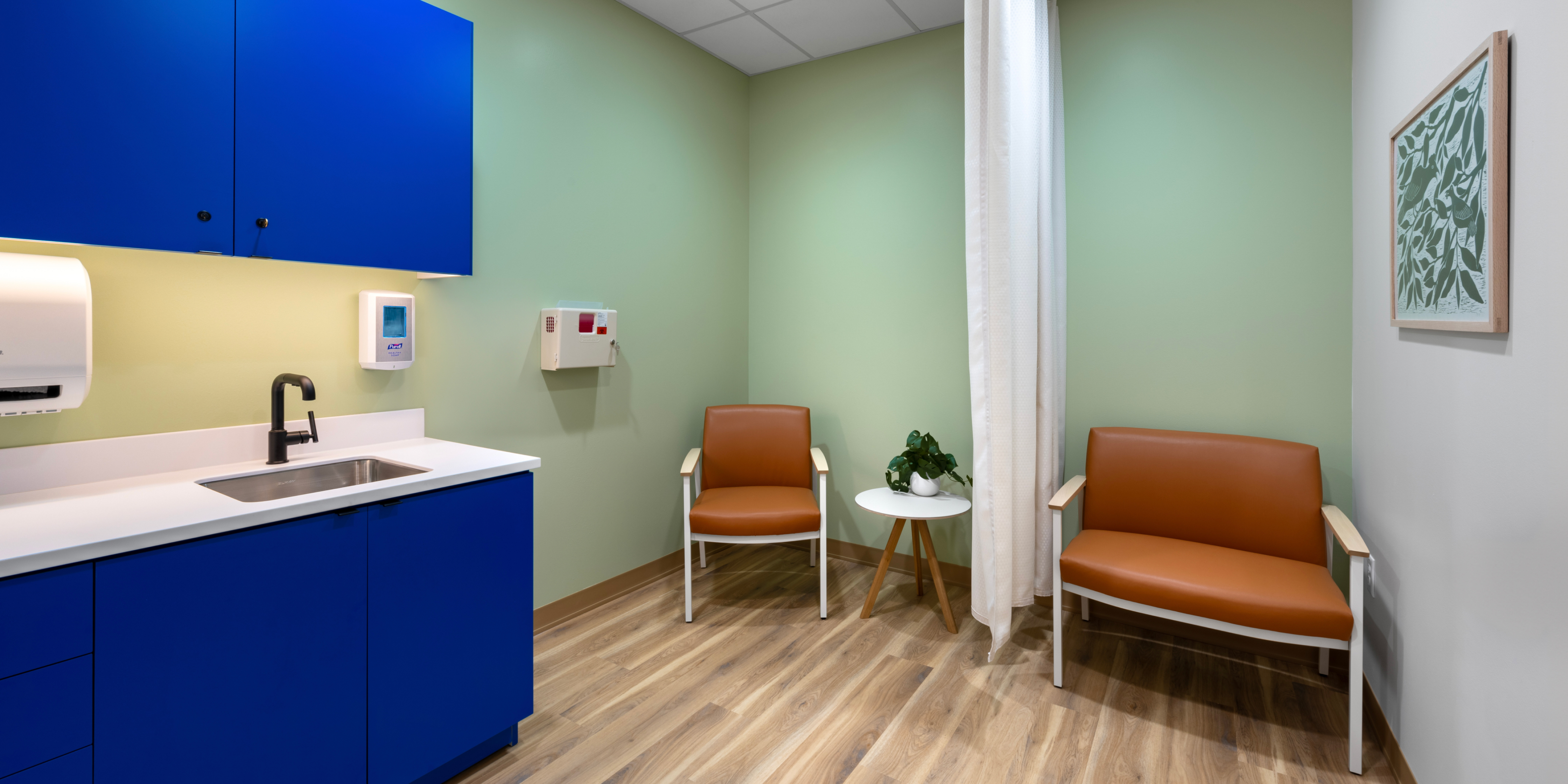 Interior of exam room with teal walls, navy blue cabinets, and tan chairs.