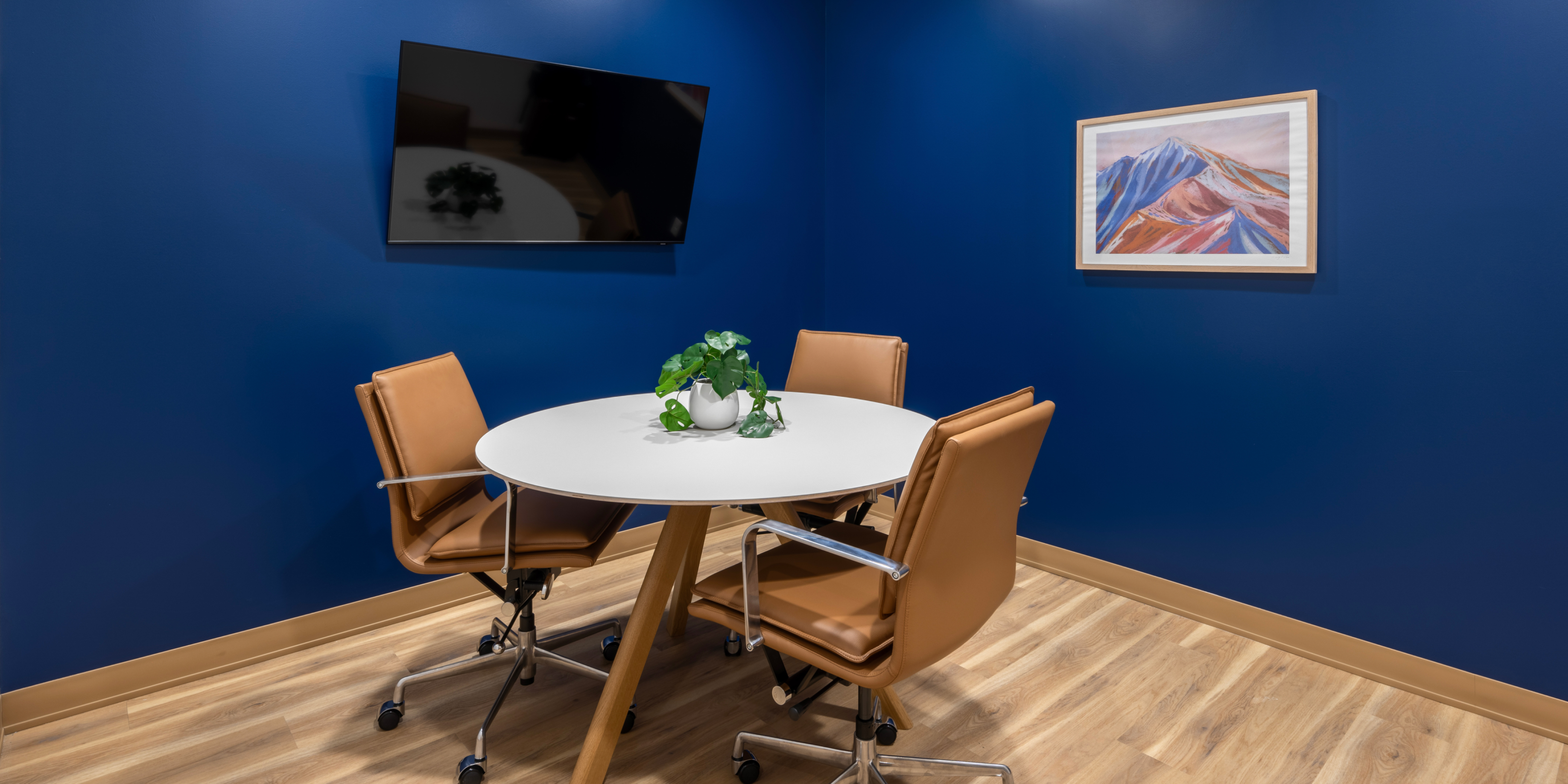 Meeting room with navy blue walls, a round table and tan rolling chairs.