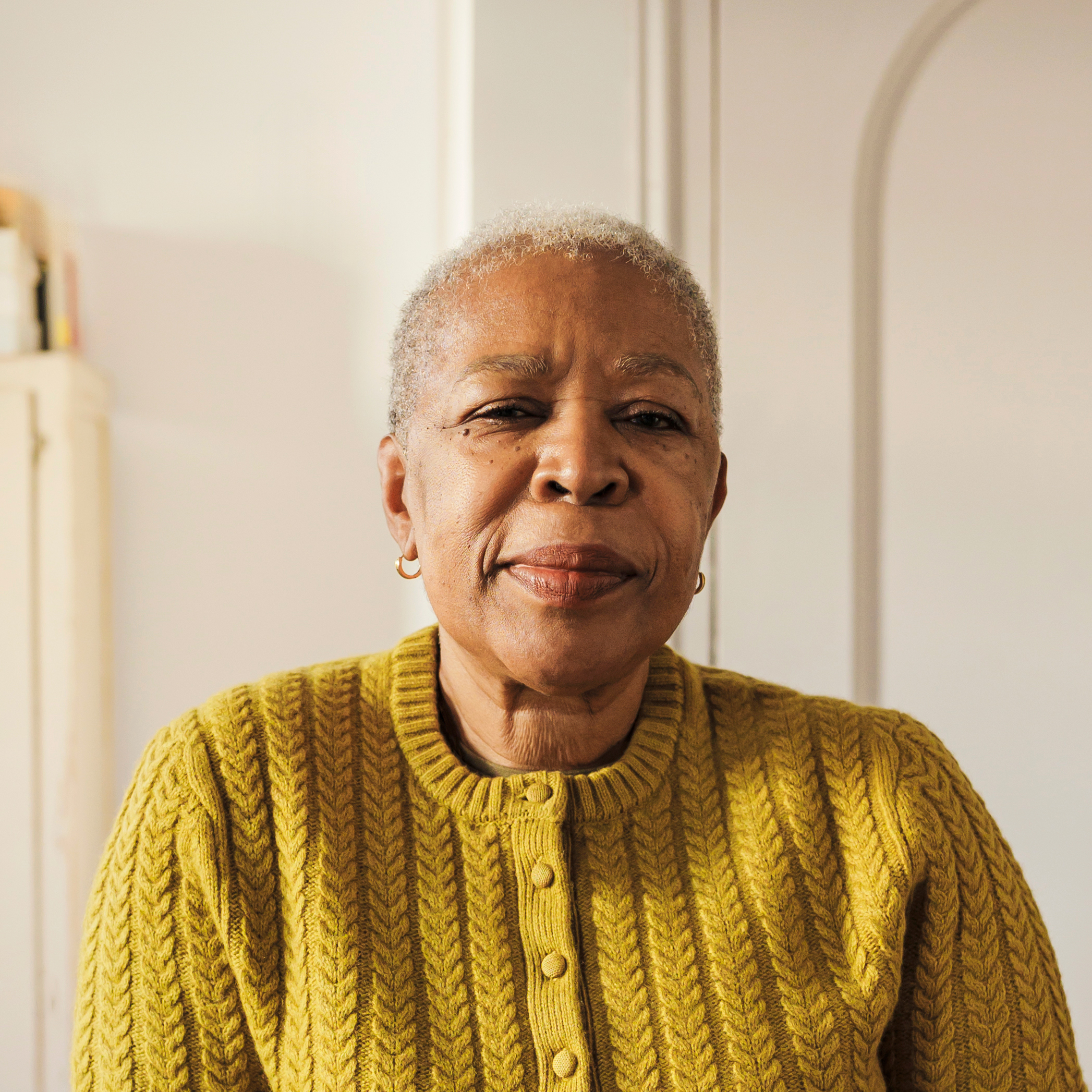 Senior woman wearing a yellow cardigan with white room background.
