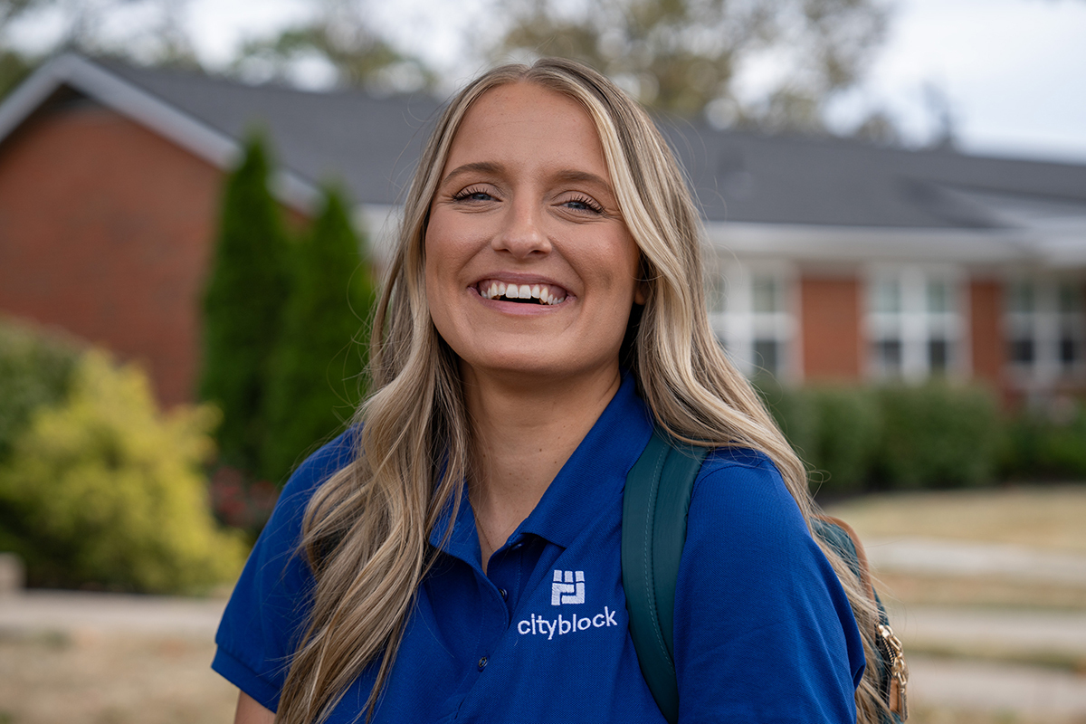 Woman with blonde hair and blue Cityblock polo smiles.