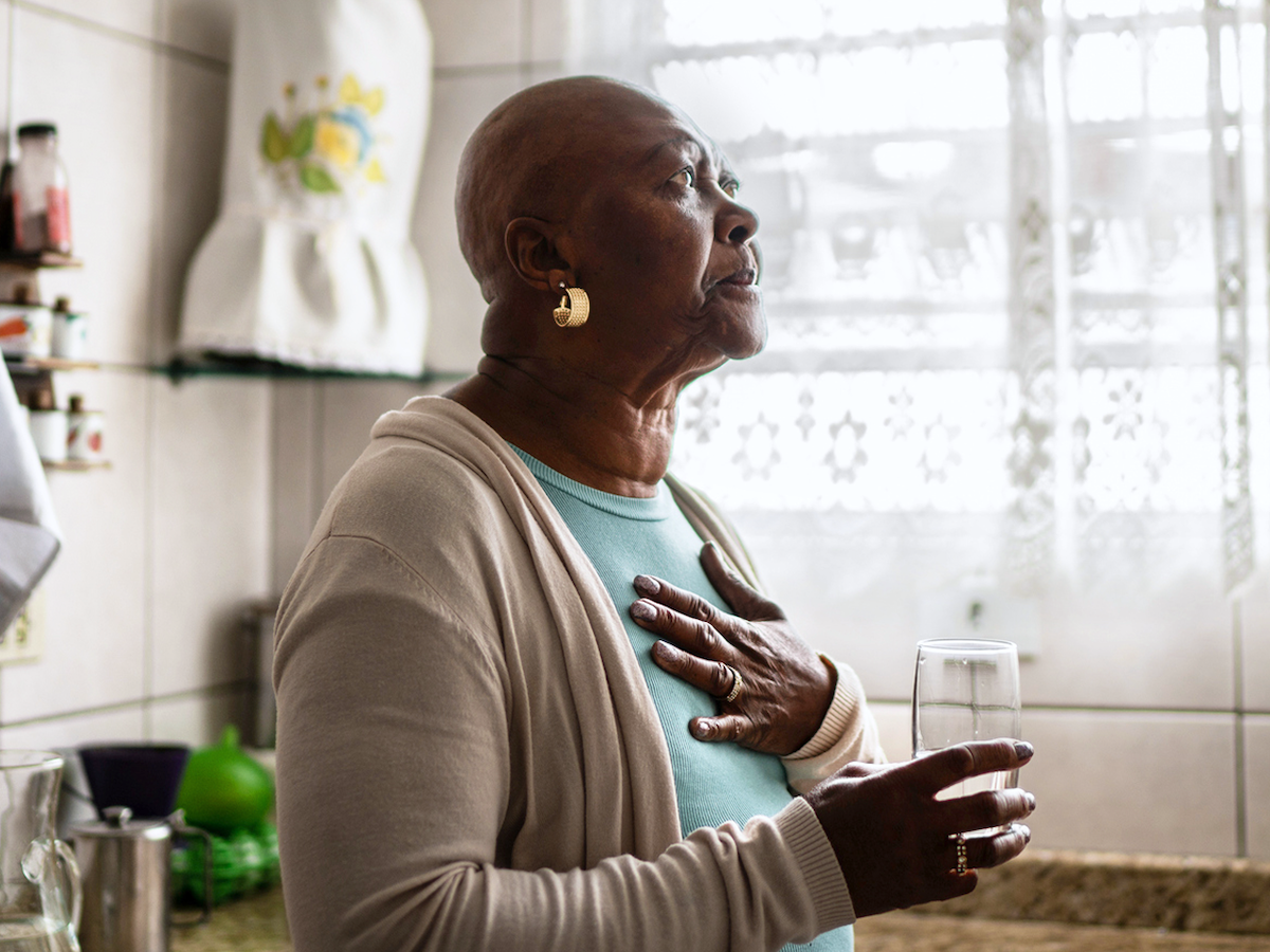 Photo of an older woman in a kitchen looking meditative with her hand on her chest