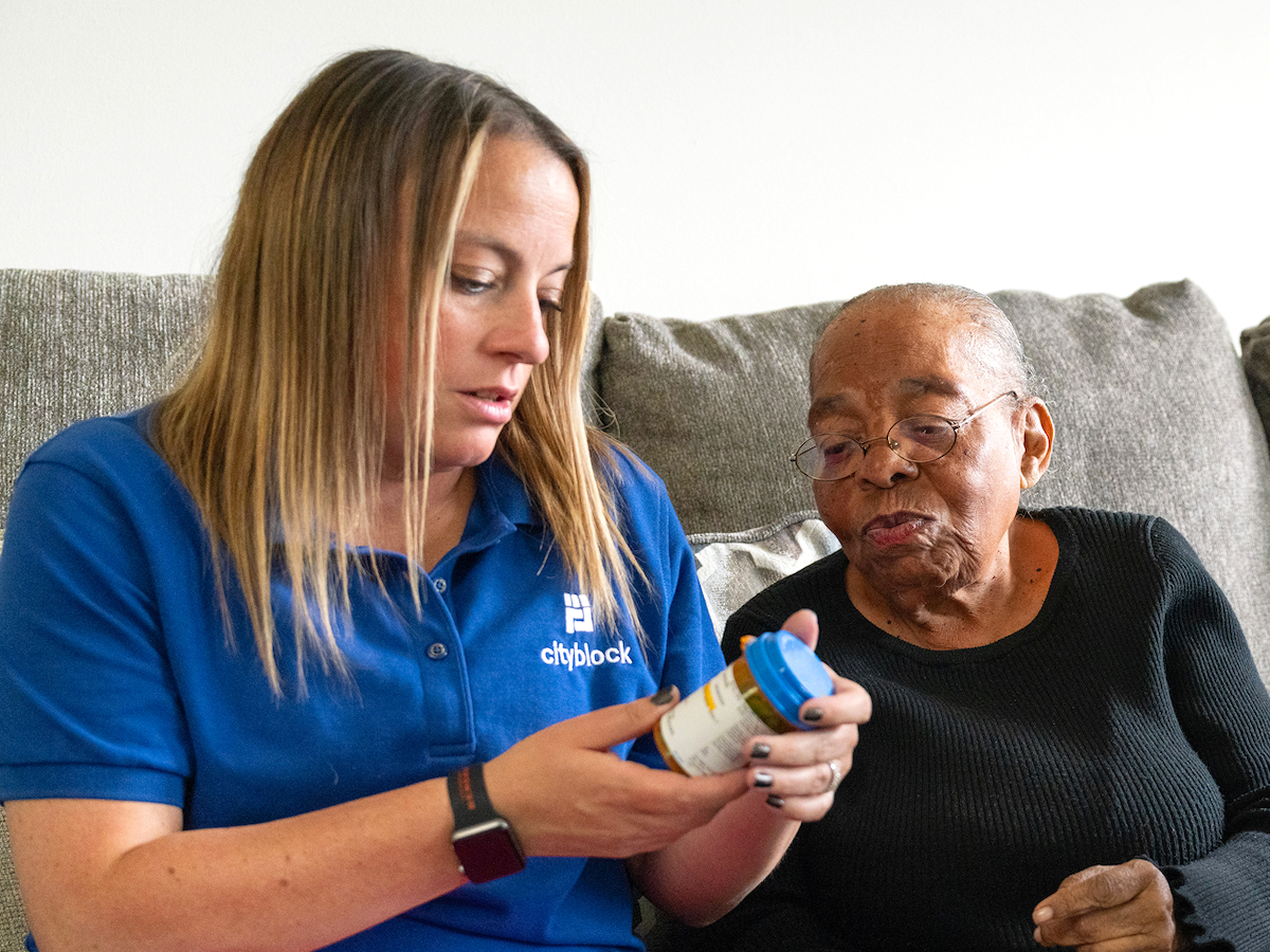 Photo of a Cityblock employee looking at a pill bottle with a member on a sofa