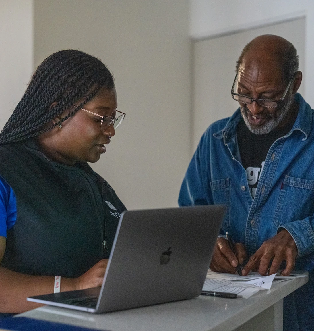 Photo of a community health partner in a Cityblock vest assisting a member who is signing papers next to a laptop.